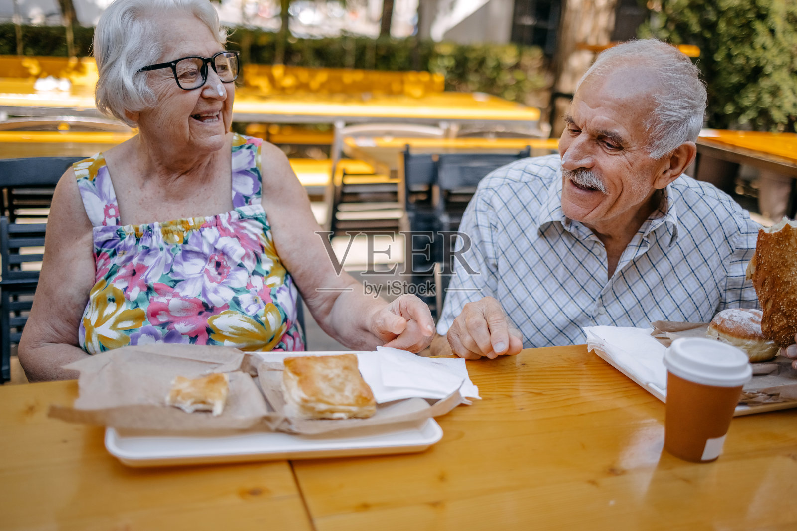 老年夫妇坐在面包店前一起吃早餐照片摄影图片