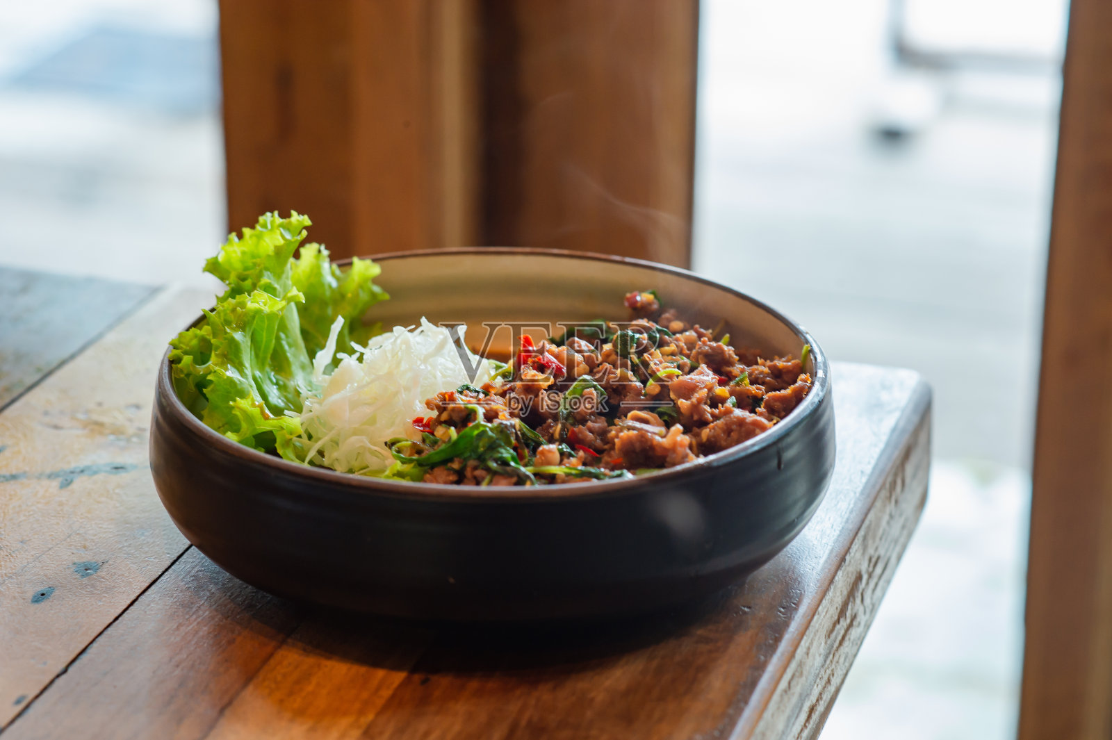 木桌上用黑色容器盛着罗勒香炒牛肉，这是餐馆里很受欢迎的菜单。照片摄影图片