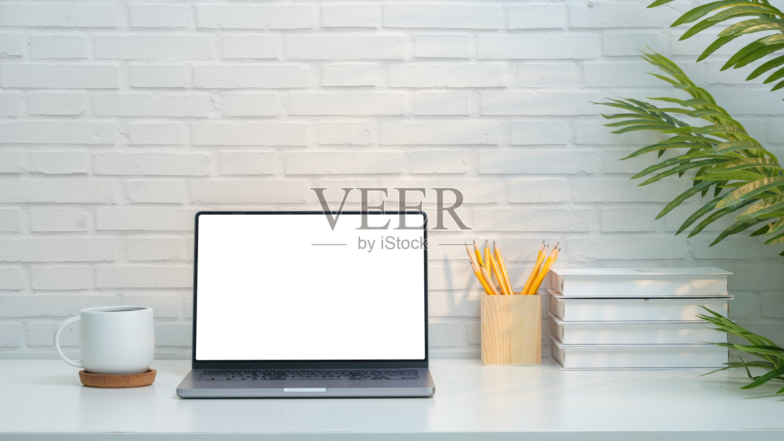 极简主义的家庭办公室设置展示了一个光滑的笔记本电脑与一个空白的白色屏幕，完美的添加自己的内容。工作空间的特点是干净。照片摄影图片