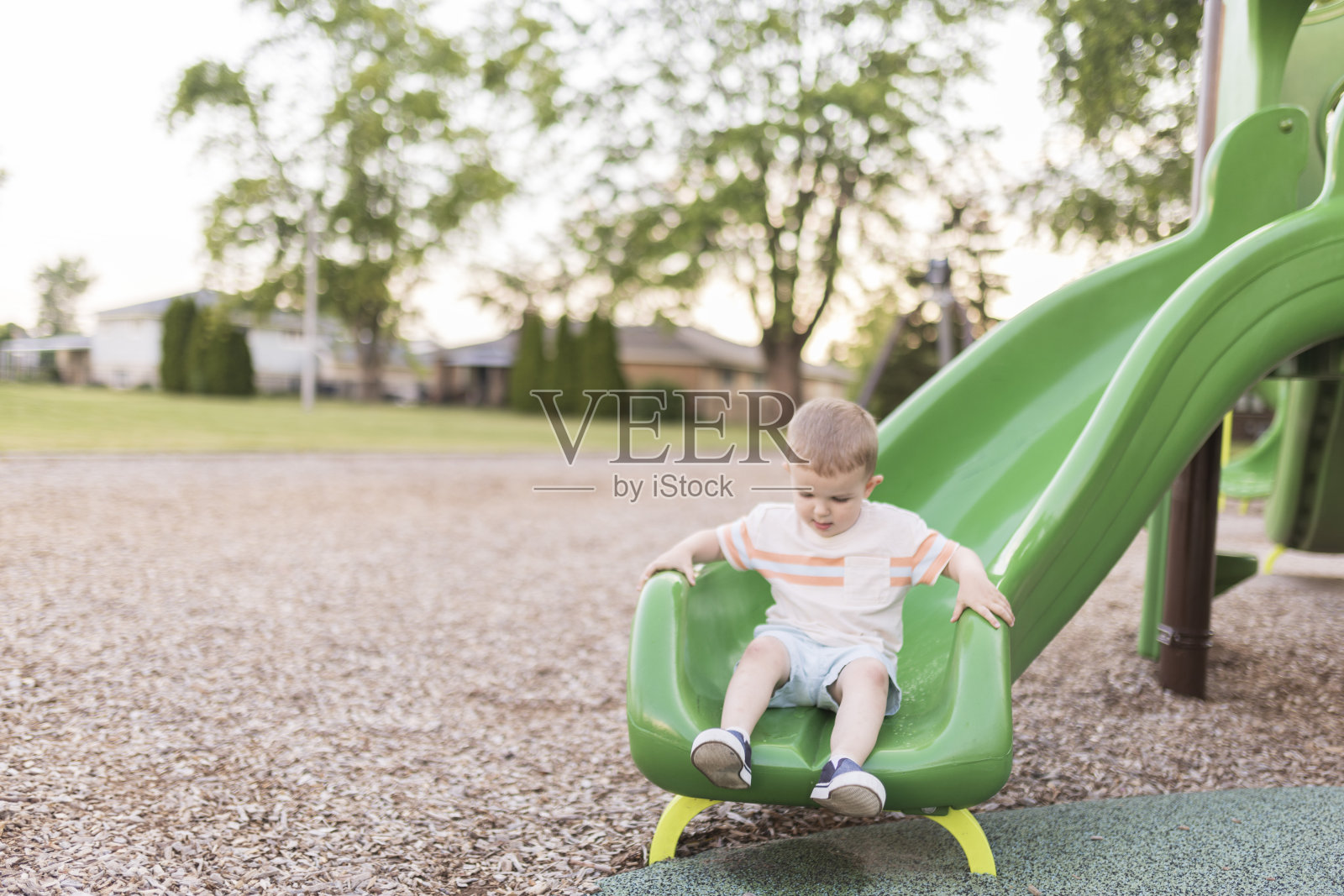 一个快乐的小男孩在操场上滑下滑梯照片摄影图片