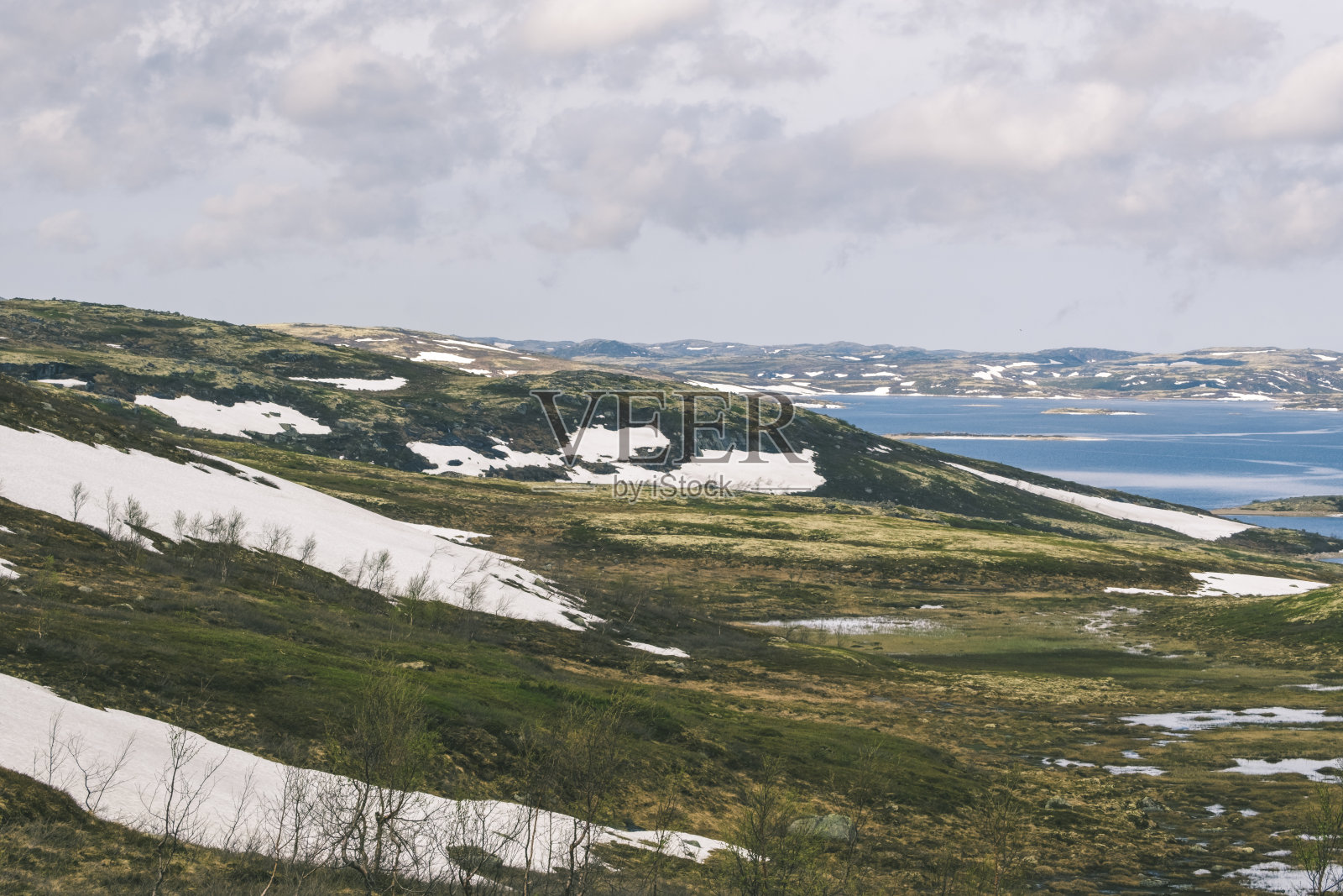 春天，宁静的湖边，连绵起伏的山丘上，宁静的雪堆。Teriberka、俄罗斯照片摄影图片