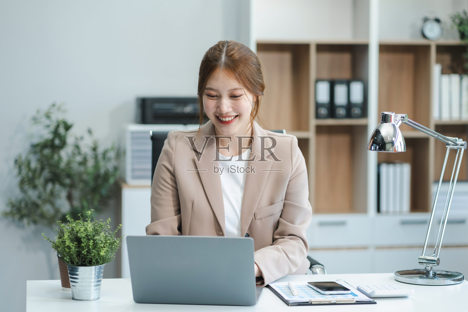 在现代办公室里，女商人用平板电脑和笔记本电脑处理办公桌上的文件。照片摄影图片