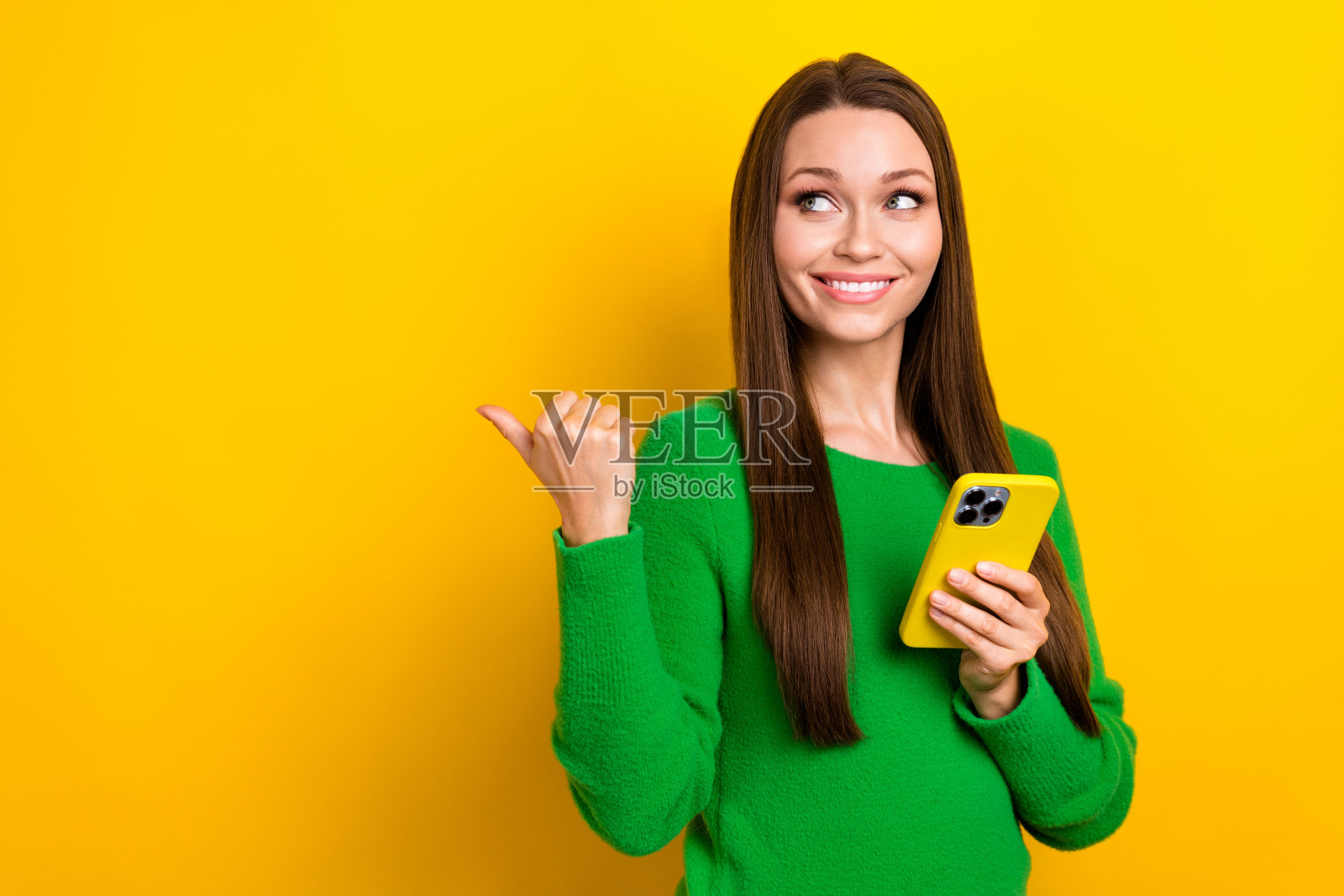 迷人的人拿着智能手机的照片，看着手指空白的空间，黄色背景上孤立的宣传照片摄影图片