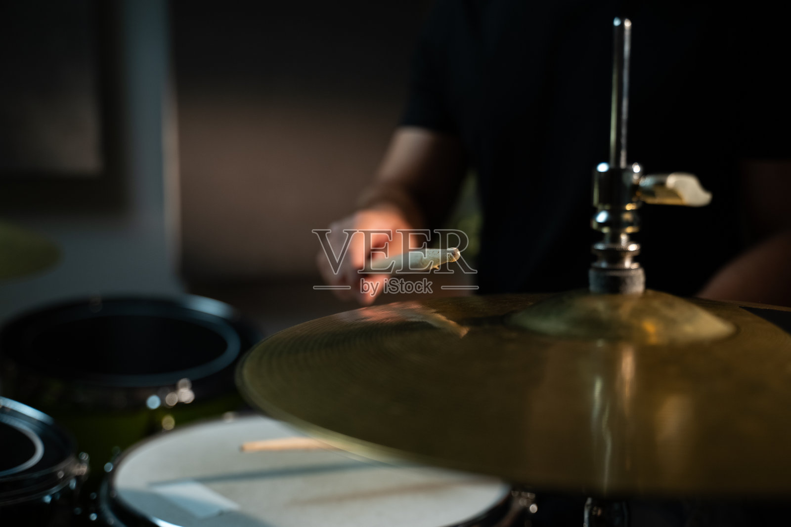 鼓手用鼓槌敲击高音帽，发出响亮、铿锵的声音。鼓手穿着黑色衬衫，铙钹又大又金。照相机的特写镜头对准盘子，捕捉撞击的瞬间。照片摄影图片