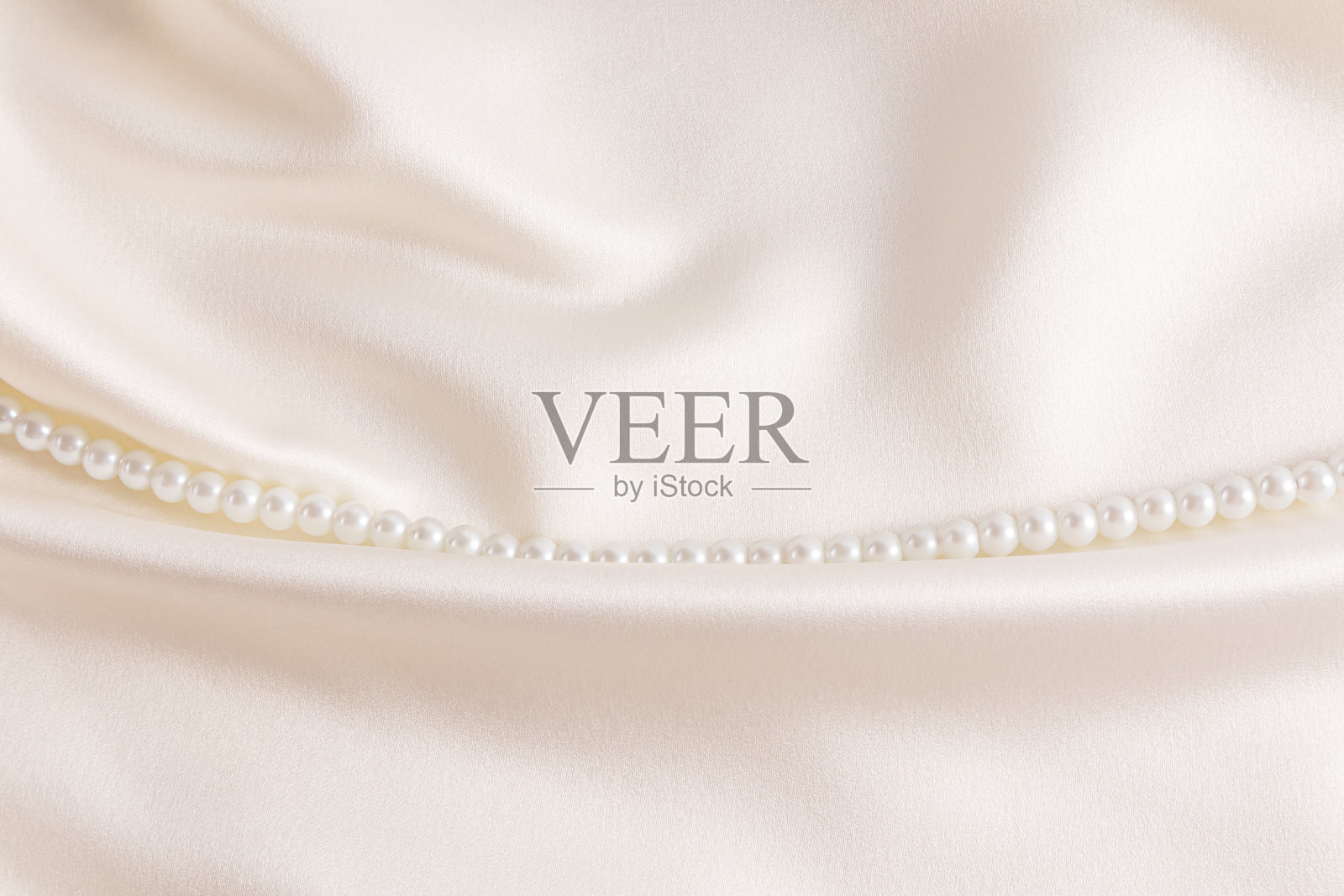 时尚现代的婚礼背景别致的米色缎面与一串白色珍珠珠从左到右折叠的织物。一个拷贝空间。照片摄影图片