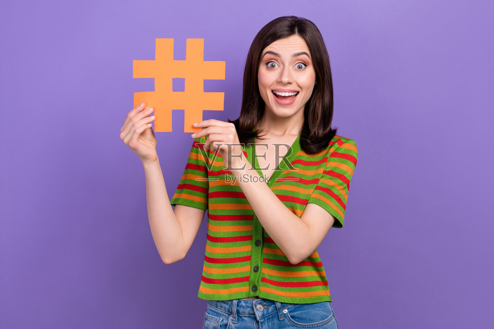照片中兴奋时髦的女人穿着条纹开衫上升哈希标签卡孤立的紫色背景照片摄影图片