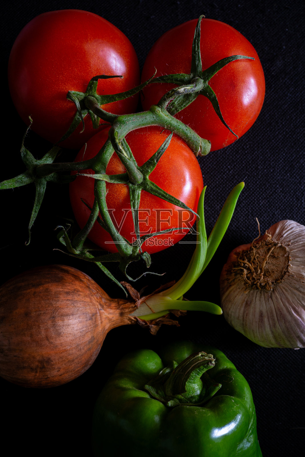 三个西红柿，一个青椒，一个蒜头和一个洋葱，背景是黑色的。照片摄影图片