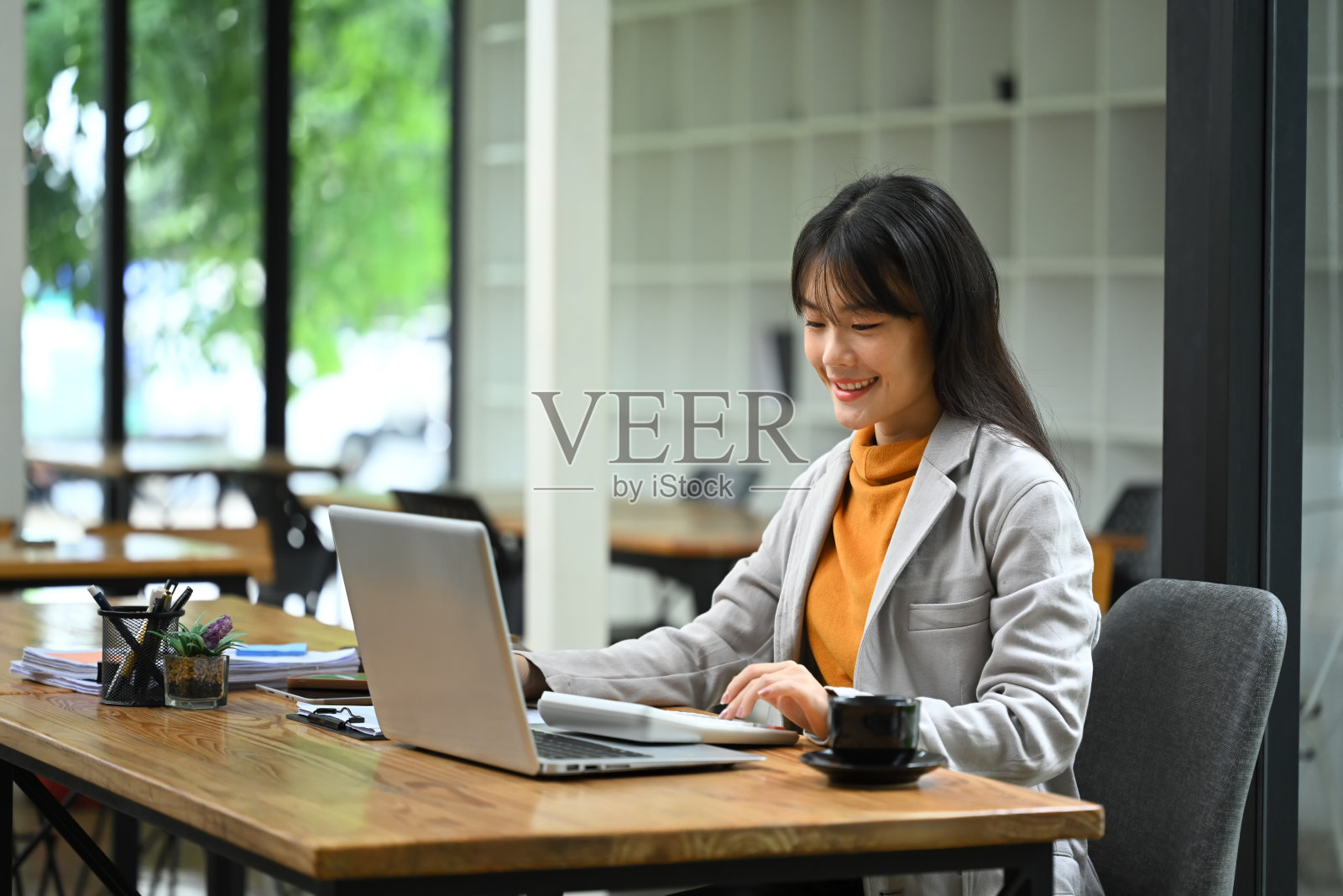 亚洲女商人坐在办公桌前，拿着笔记本电脑，用计算器分析财务文件照片摄影图片