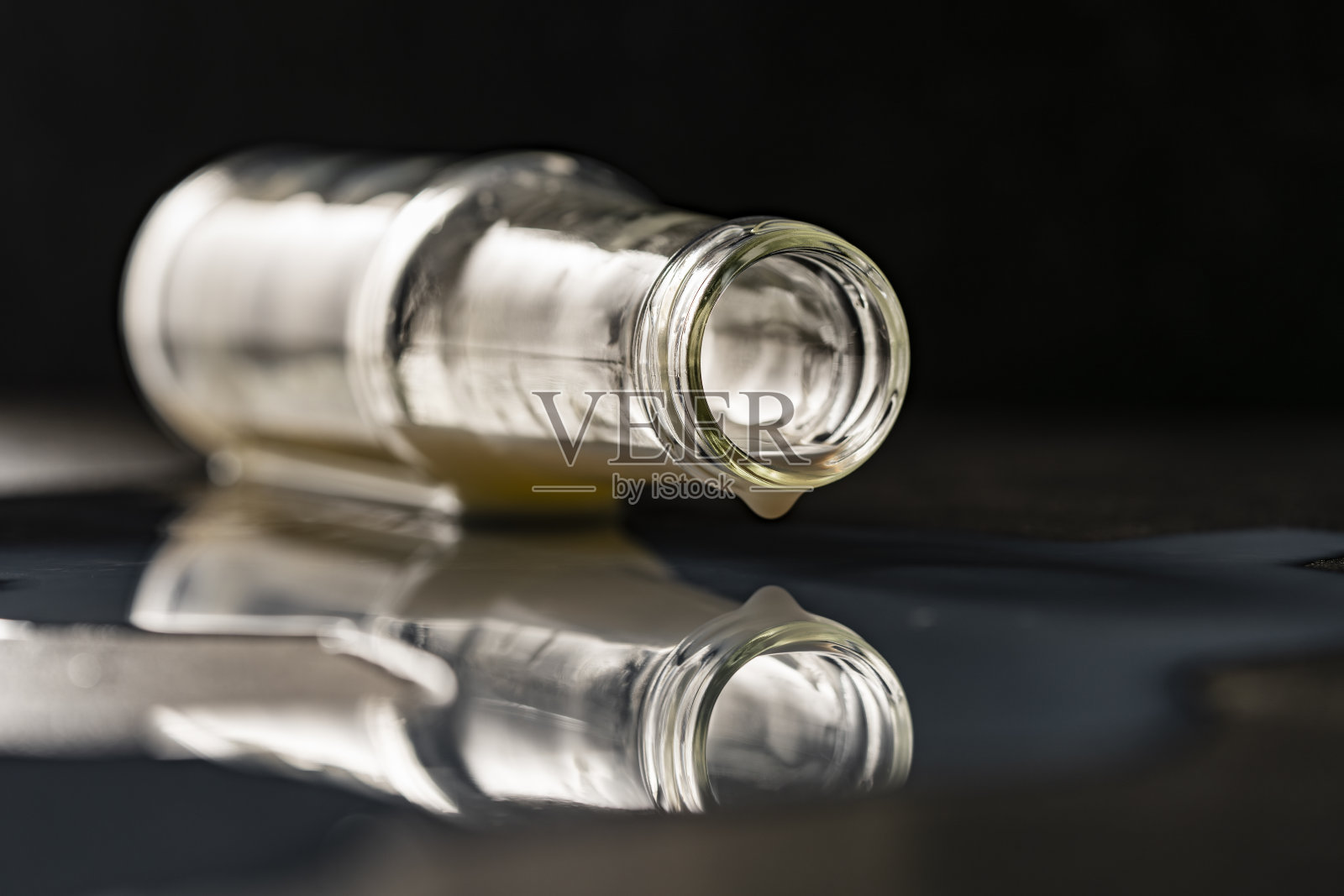 黑色背景上洒着牛奶的玻璃瓶，特写照片摄影图片