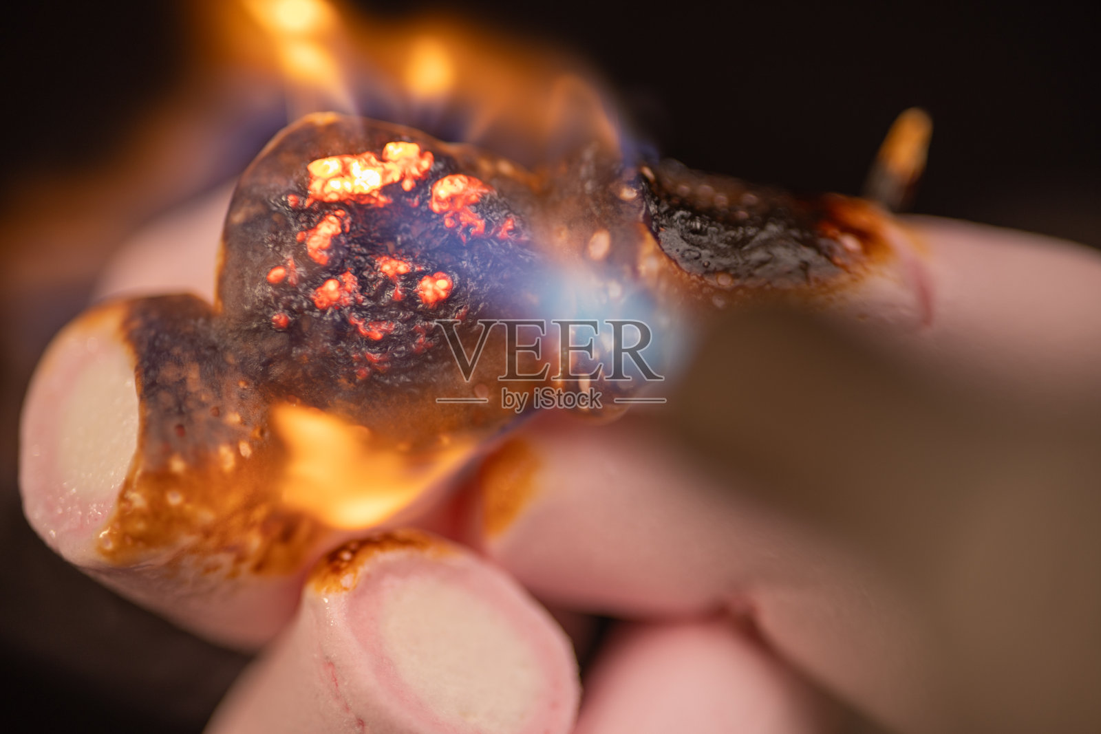 目睹棉花糖屈服于火炬的高温。黑色的背景使融化过程看起来戏剧性和迷人。照片摄影图片