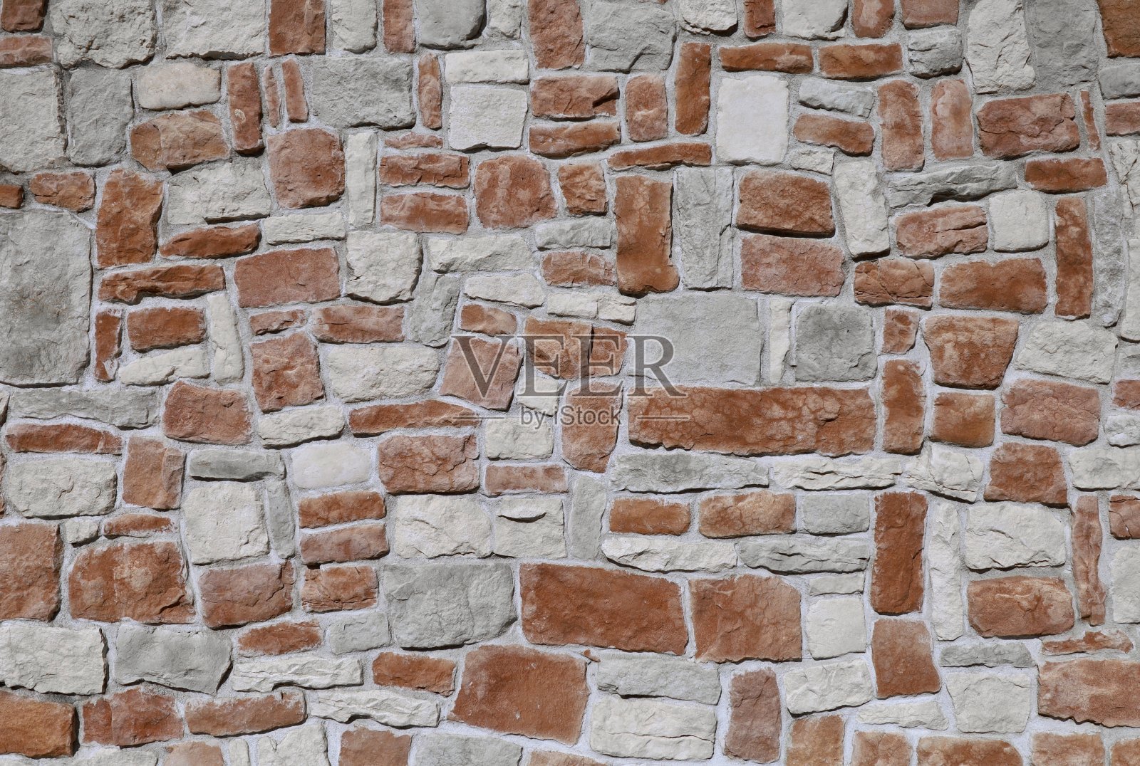 外墙覆盖层由不同形状的石头随意排列在混凝土上。颜色有棕色、灰色和白色照片摄影图片