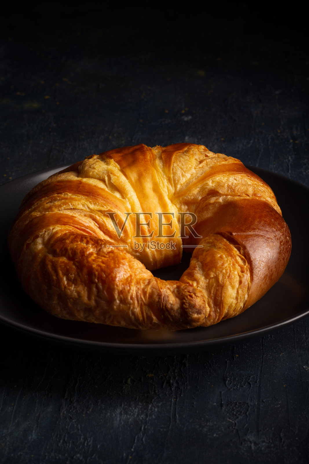 黑色盘子上的金色诱人羊角面包特写。照片摄影图片