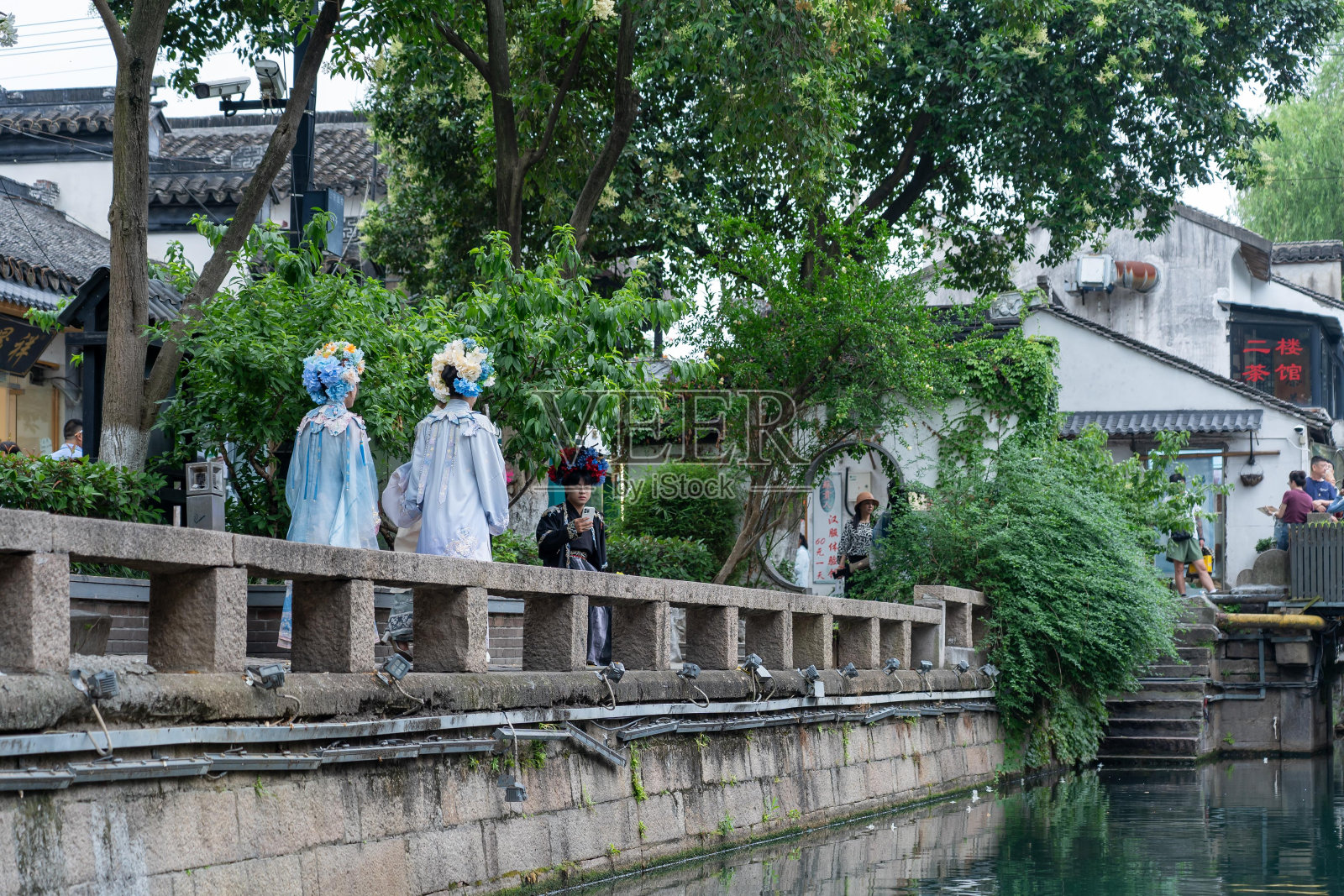 中国城市里的一条运河，有一道石墙，边上有一系列的灯。穿着传统服装的妇女沿着小路走着。照片摄影图片