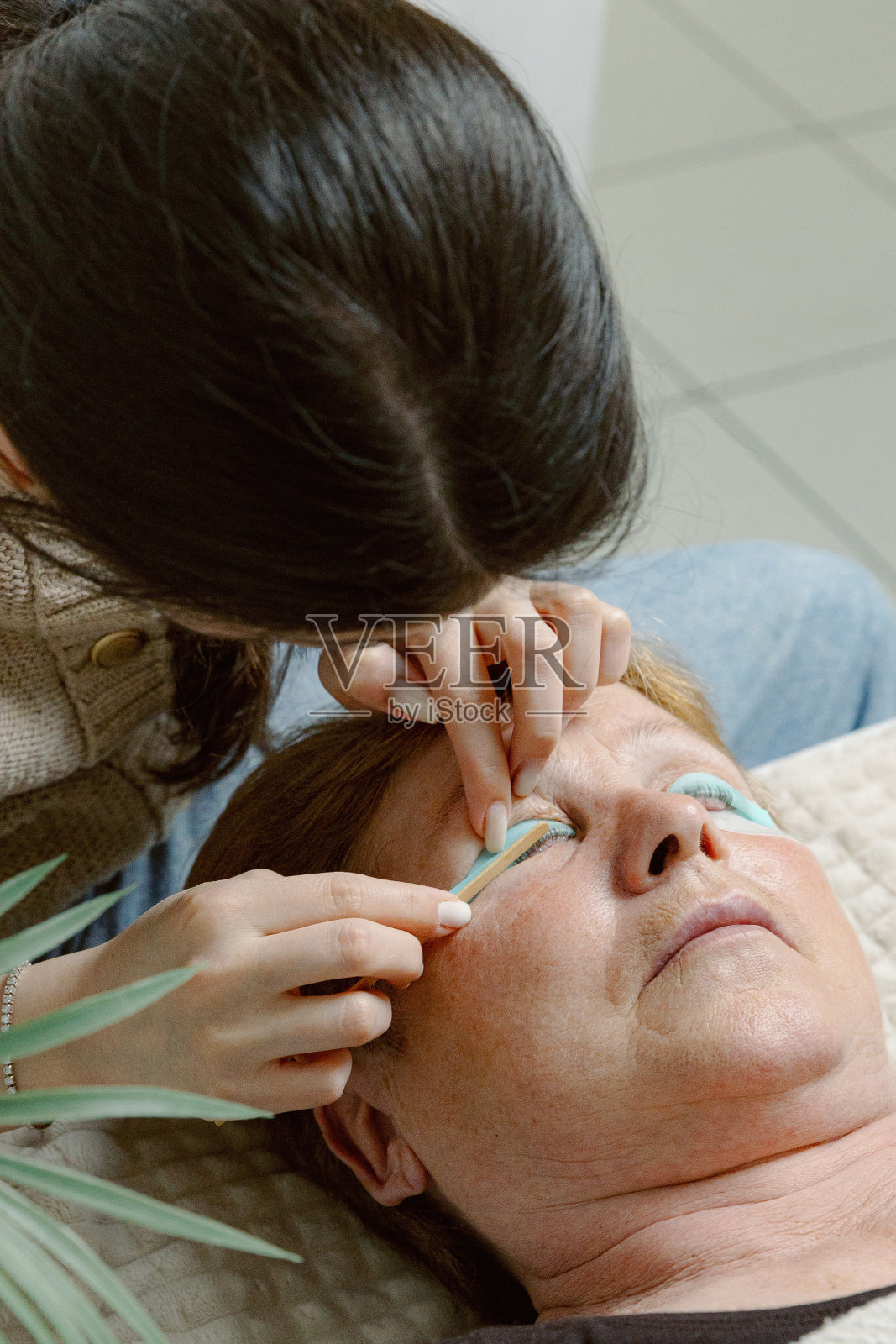 一位女美容师在给女性的睫毛贴膜。照片摄影图片
