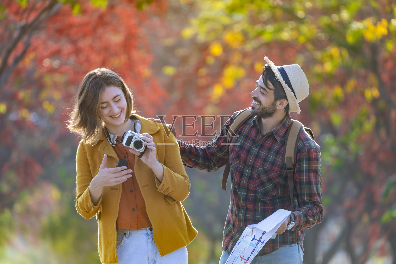 幸福的高加索夫妇在秋天的公园里与枫树和山毛榉树一起散步，看着相机拍摄的秋天彩色旅行目的地和家庭幸福照片摄影图片