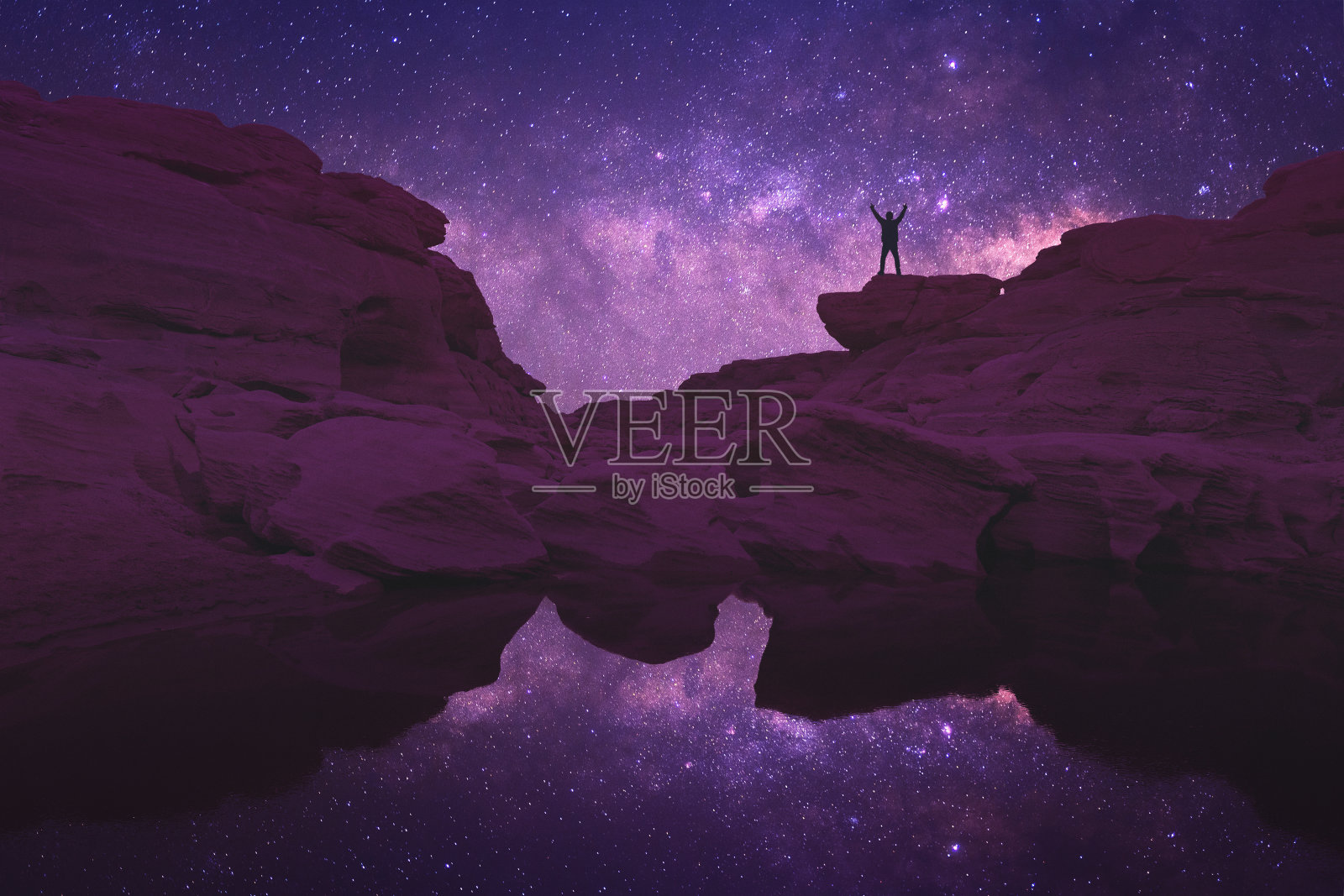 黄昏时，站在岩石上的人对着天空的低角度视角照片摄影图片