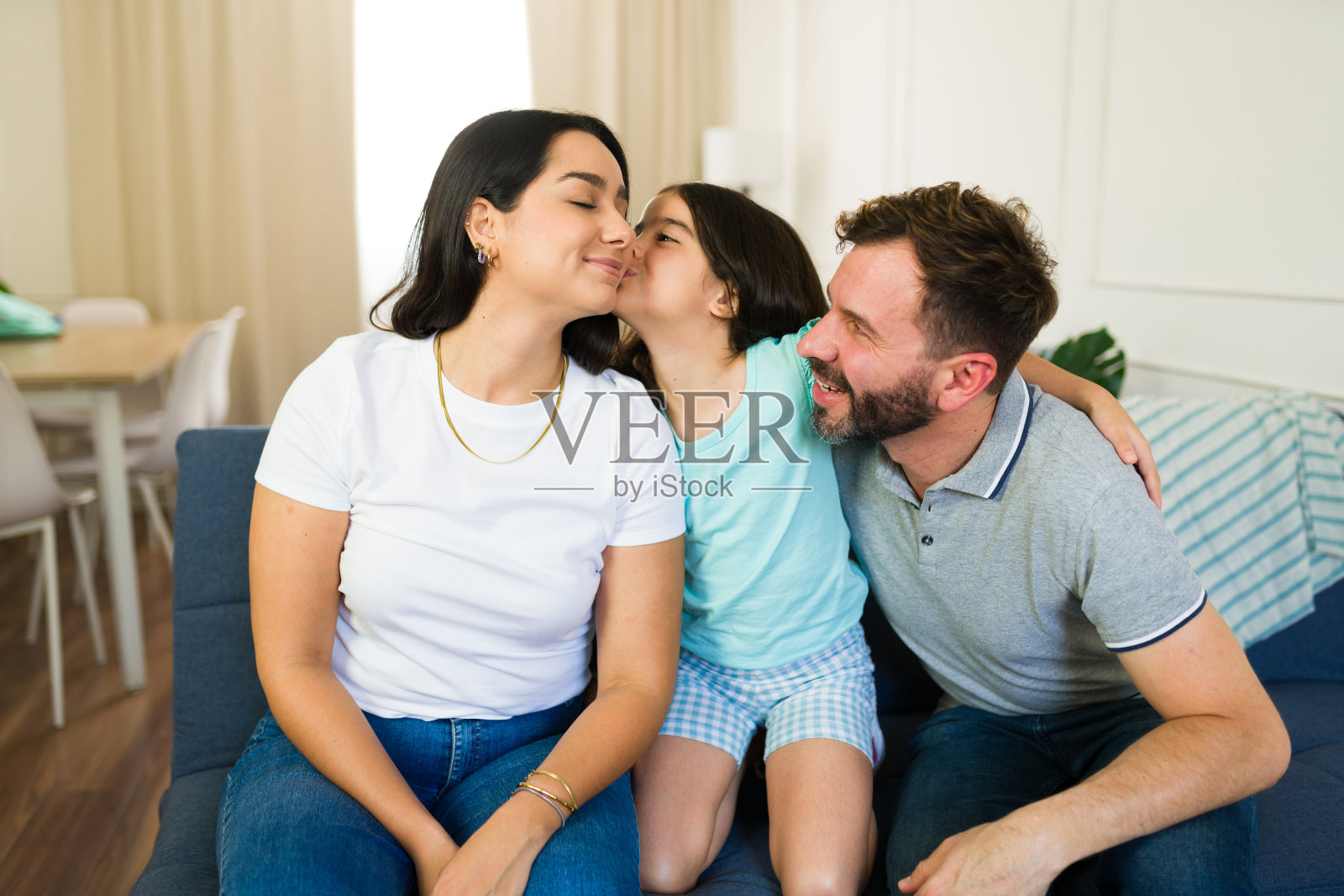 小女孩和爸爸坐在客厅的沙发上，在妈妈的脸颊上吻了一下照片摄影图片