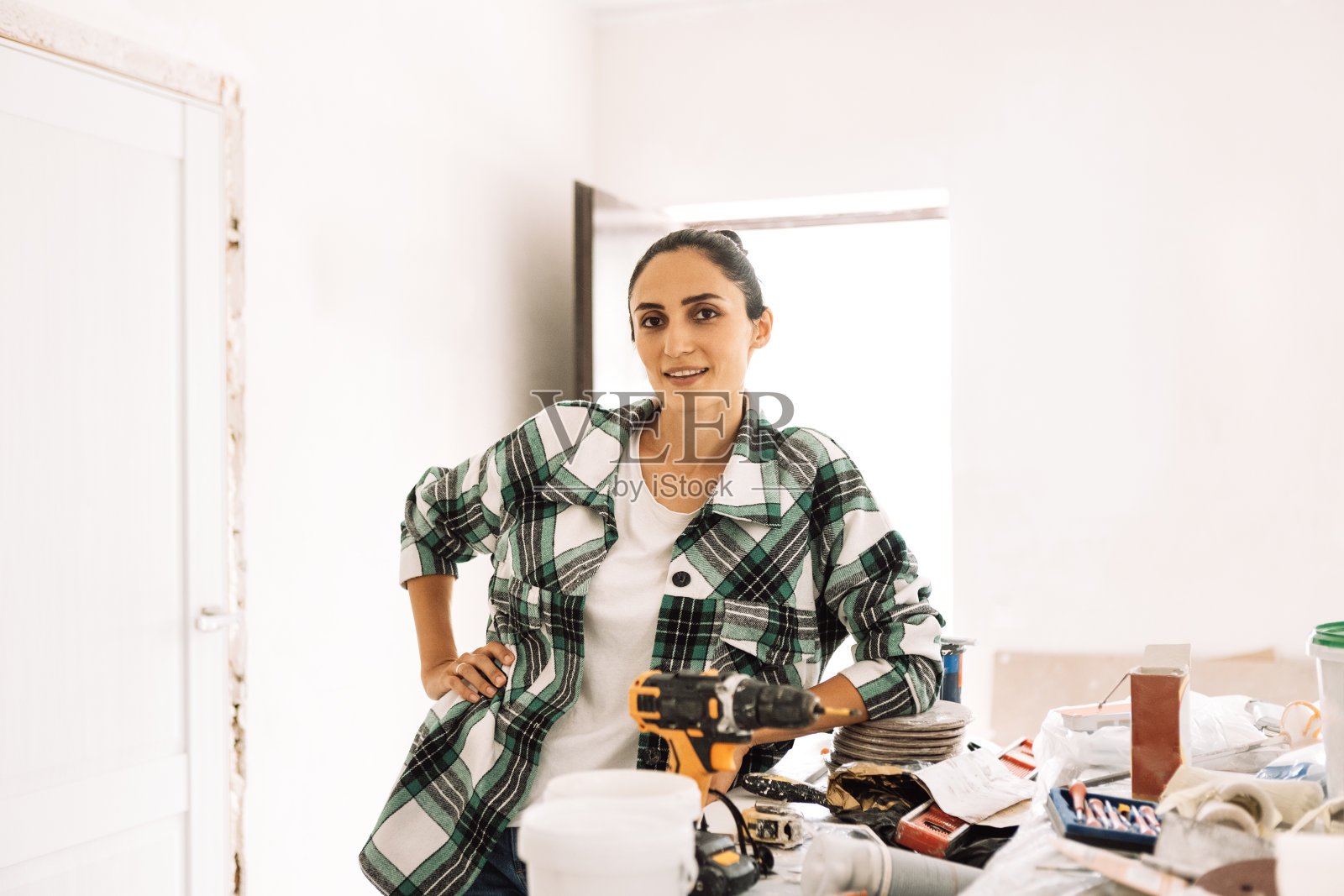 一位年轻女子站在一张桌子旁，手里拿着施工工具。一个穿着便服的迷人女孩正在公寓里修理。照片摄影图片
