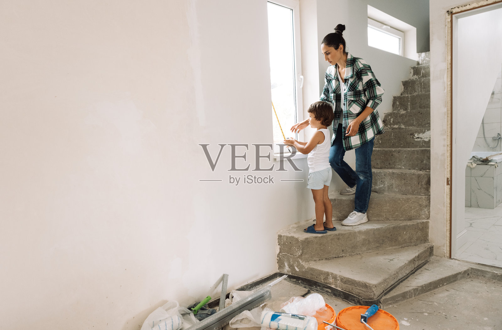 小男孩帮他妈妈量窗户开口的长度。年轻女子和她可爱的儿子在建筑工具和材料旁边。照片摄影图片