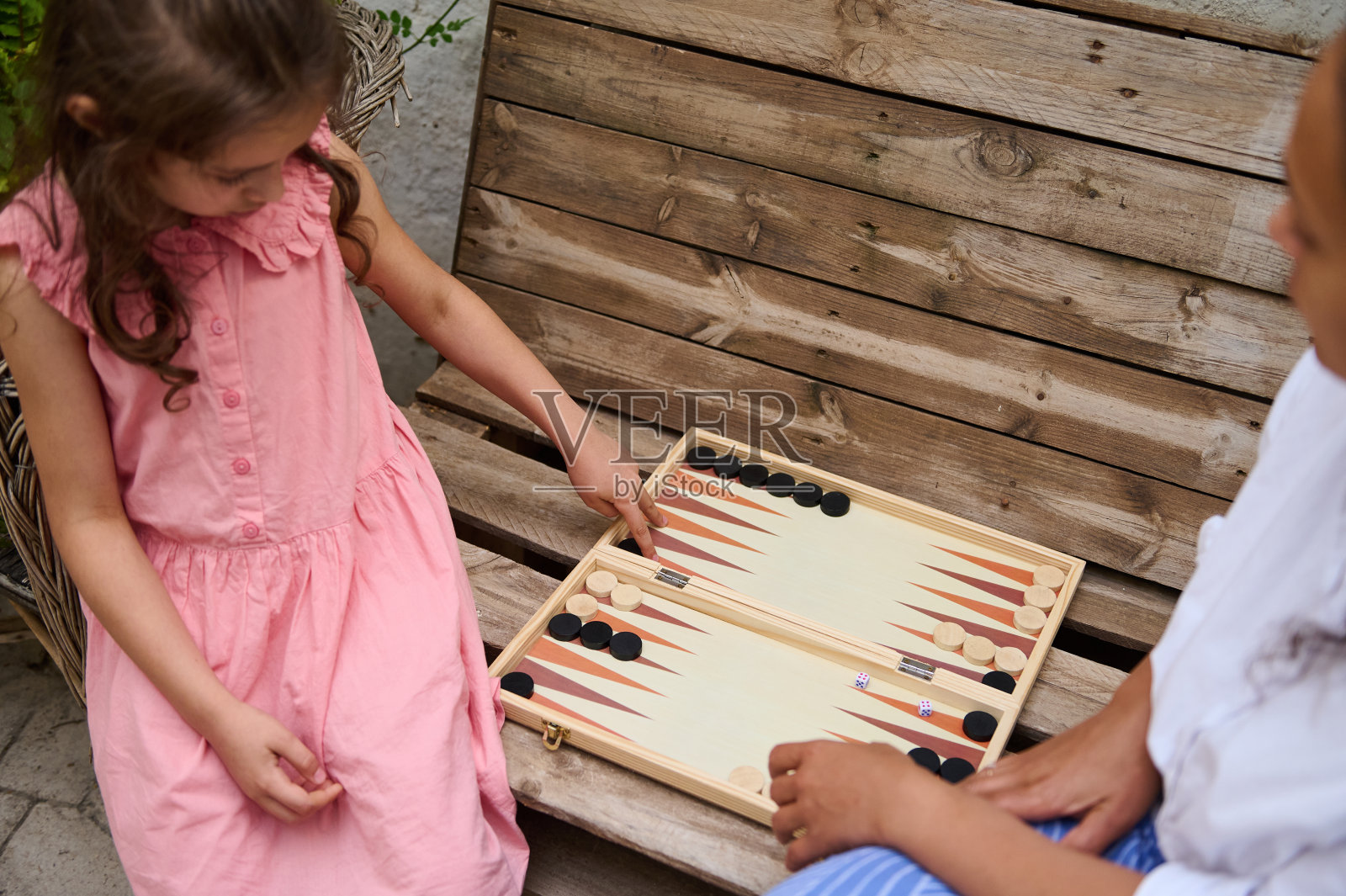 小女孩和大人在木凳上玩西洋双陆棋，一家人在户外团聚照片摄影图片