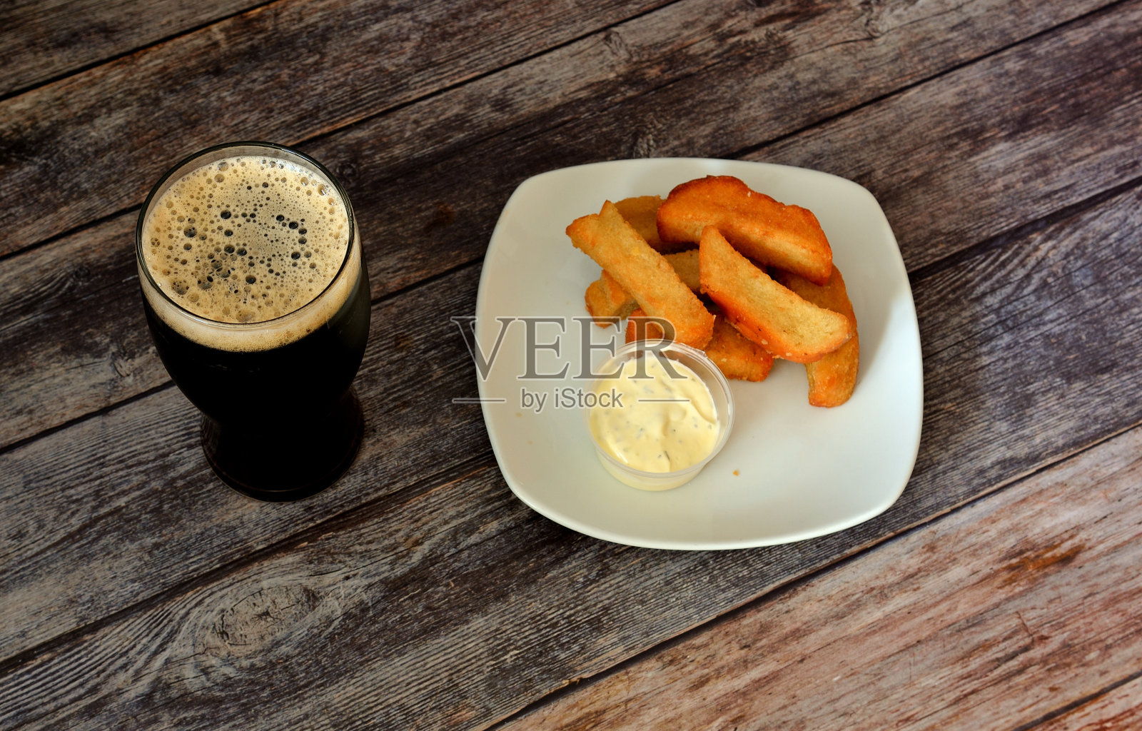 一大杯黑啤酒，木桌上放着一盘小麦面包丁和酱汁。照片摄影图片