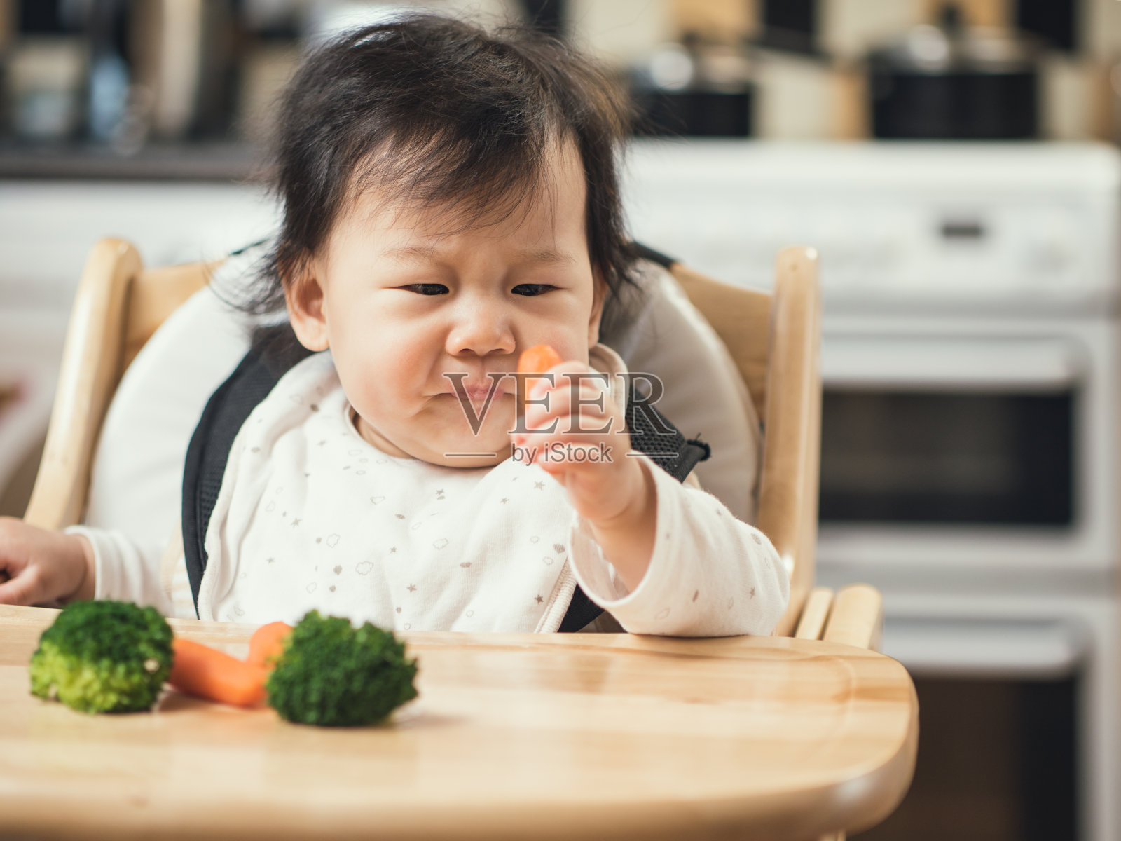 小女孩坐在家里的高脚椅上拿着胡萝卜照片摄影图片