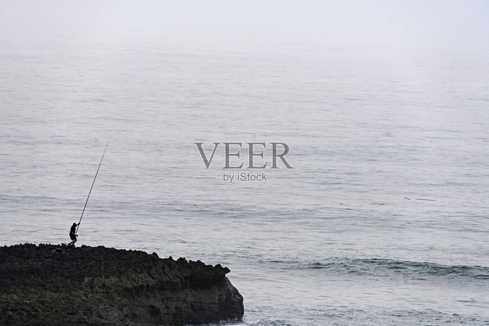 多雾条件下岩石海岸线上孤独的渔夫照片摄影图片