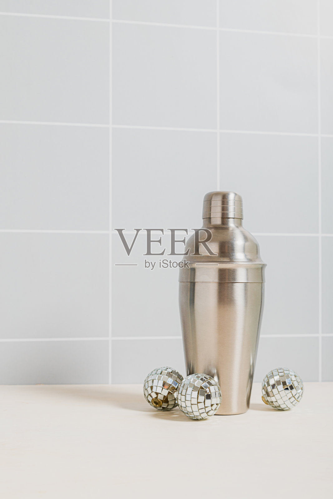 银色鸡尾酒摇壶，上面有小小的迪斯科球。灰方格墙照片摄影图片
