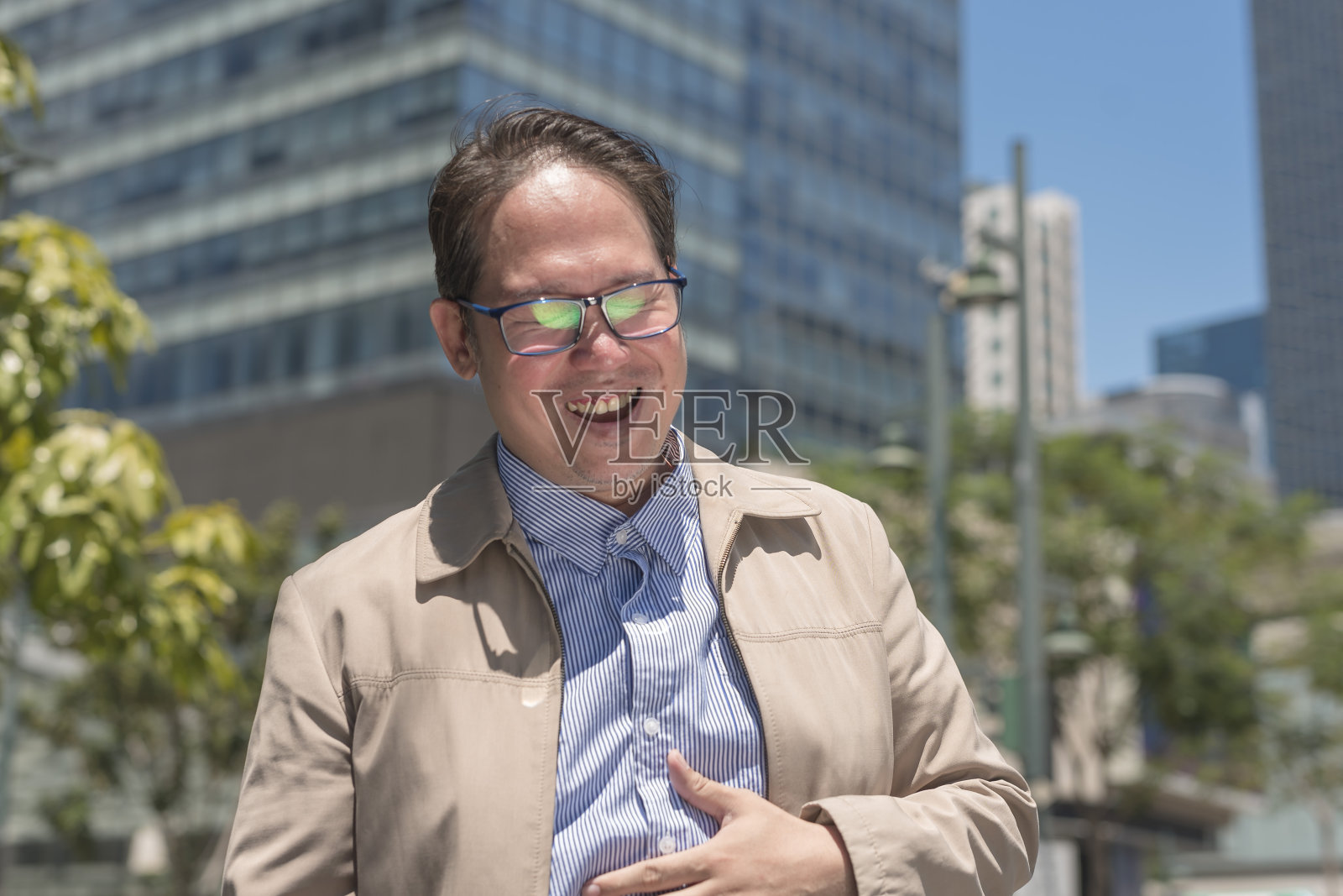 一个40多岁的中年上班族，笑得无法控制，很开心，很开心。站在外面，背景是办公大楼。照片摄影图片