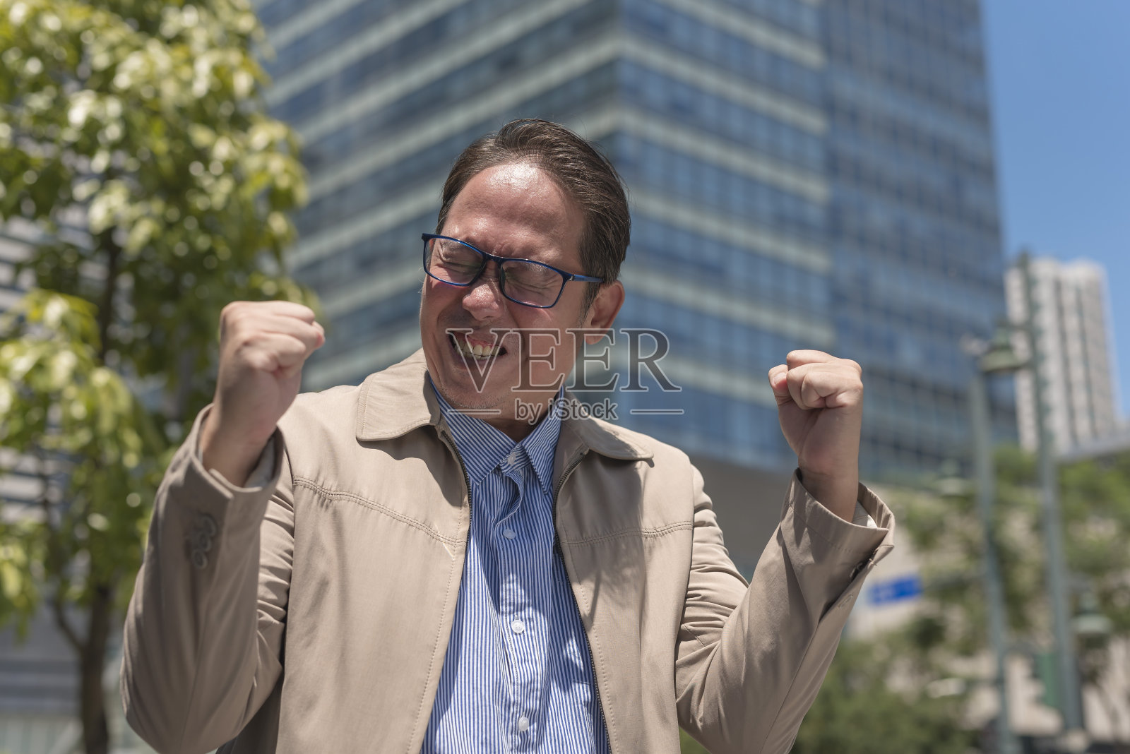 一个兴高采烈的中年男子成功地挥舞着双拳。在被提升为高级管理职位后，在外部做出反应。户外城市场景。照片摄影图片