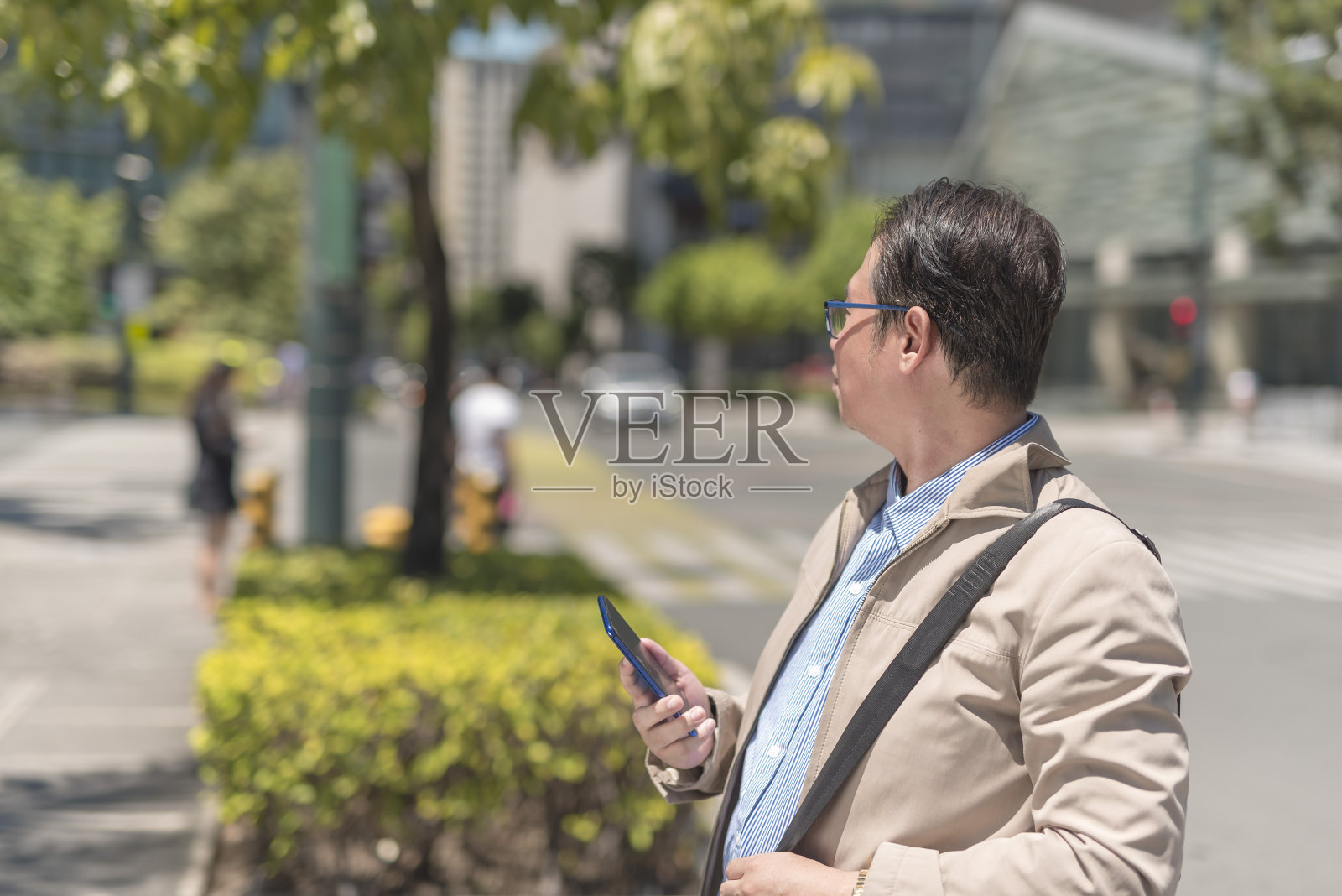 一位看似迷路的中年亚洲男子用手机上的gps地图应用程序环顾四周。在炎热的晴天里在城市里散步。照片摄影图片