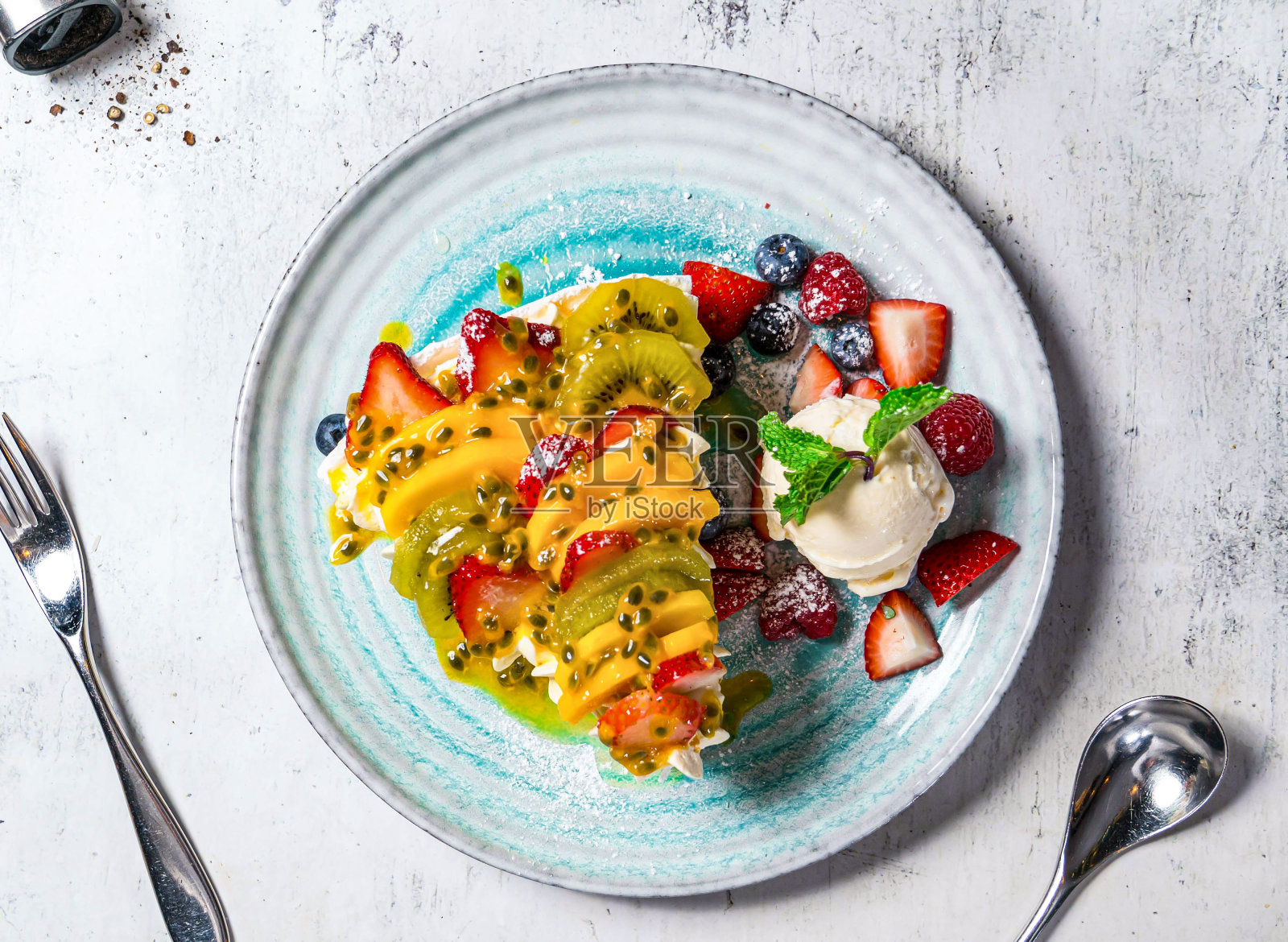 澳大利亚巴甫洛娃，配上猕猴桃、芒果、草莓、蓝莓、薄荷和香草冰淇淋，装在盘子里照片摄影图片