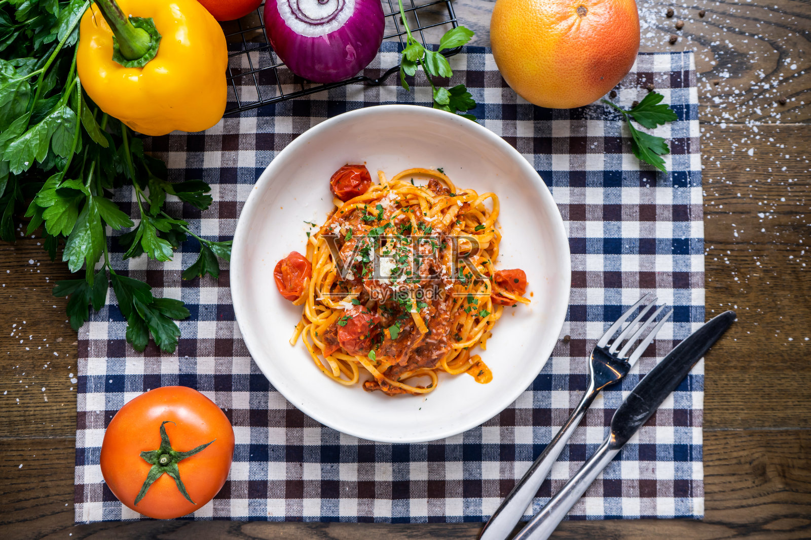 意式番茄面，配以番茄、洋葱、辣椒、香菜、刀叉，用餐巾纸隔开。木质餐桌上的意大利快餐照片摄影图片
