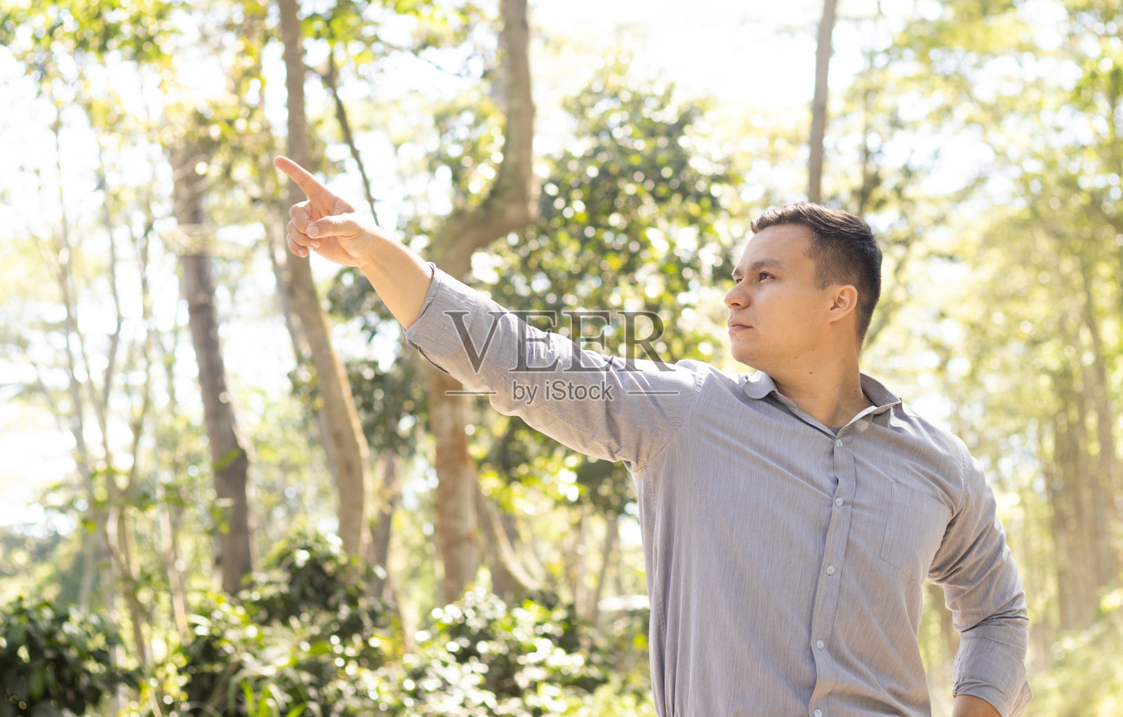年轻的拉丁男子在大自然中微笑着指着相机照片摄影图片