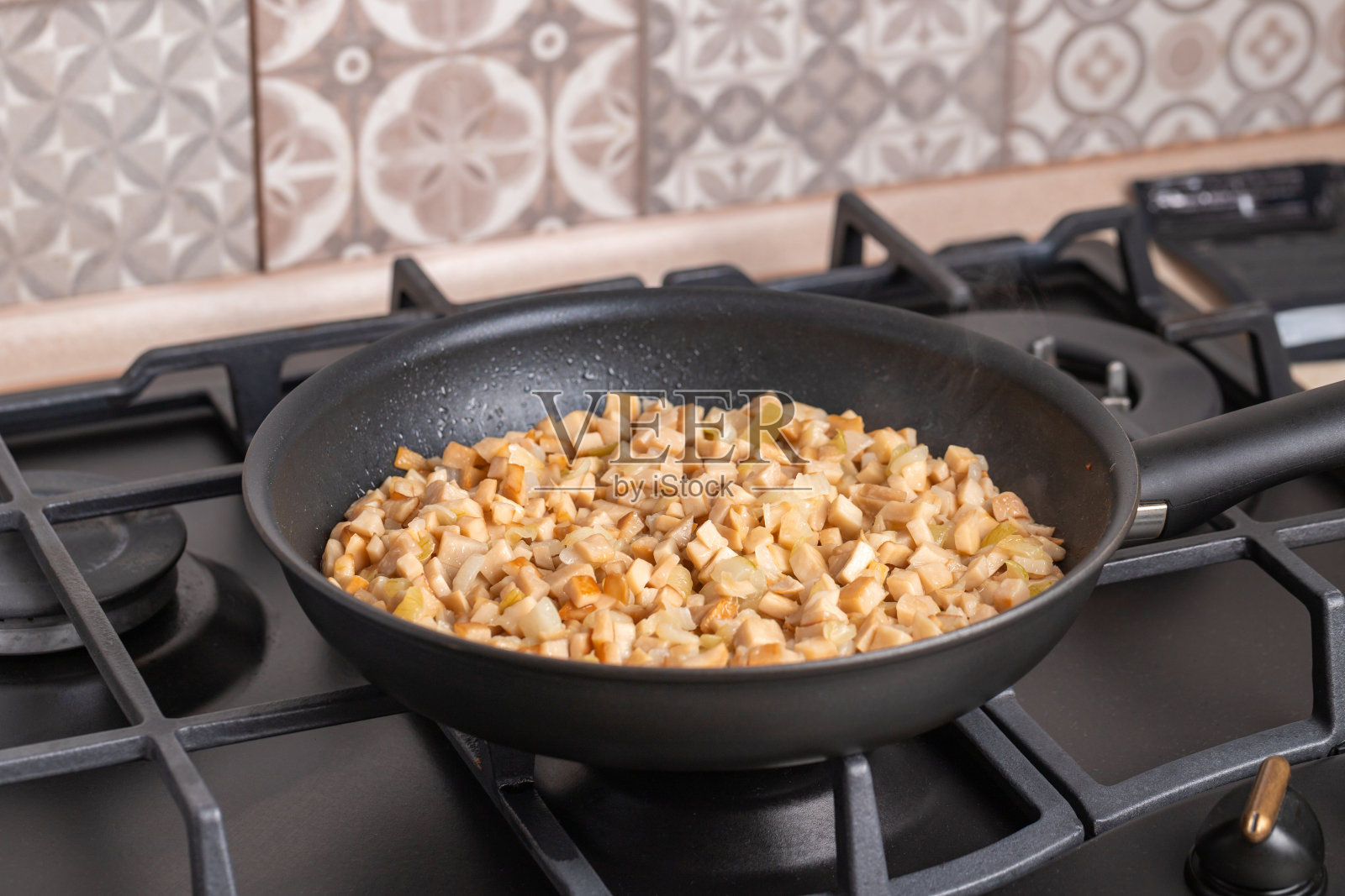 用煎锅煎蘑菇。在煎炸的过程中，在煎锅里放满切碎的新鲜的香菇和香菇或王蚝菇或凤尾菇(凤尾菇)。背景是煤气炉。照片摄影图片