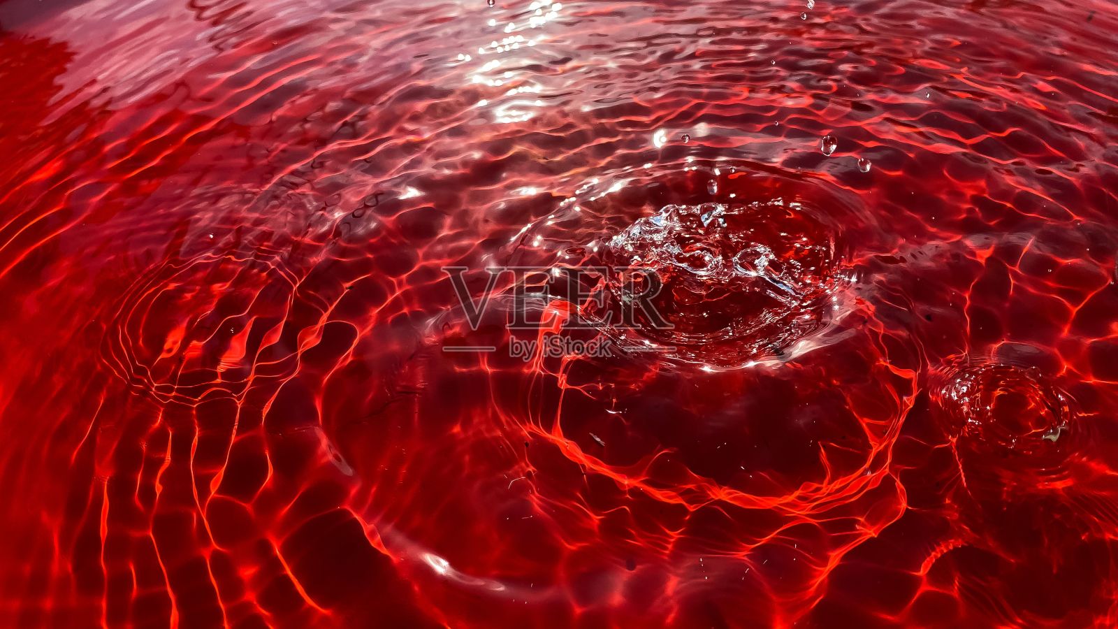 特写镜头中，雨滴落在红色的背景上，在水面上留下一个个圆圈。照片摄影图片