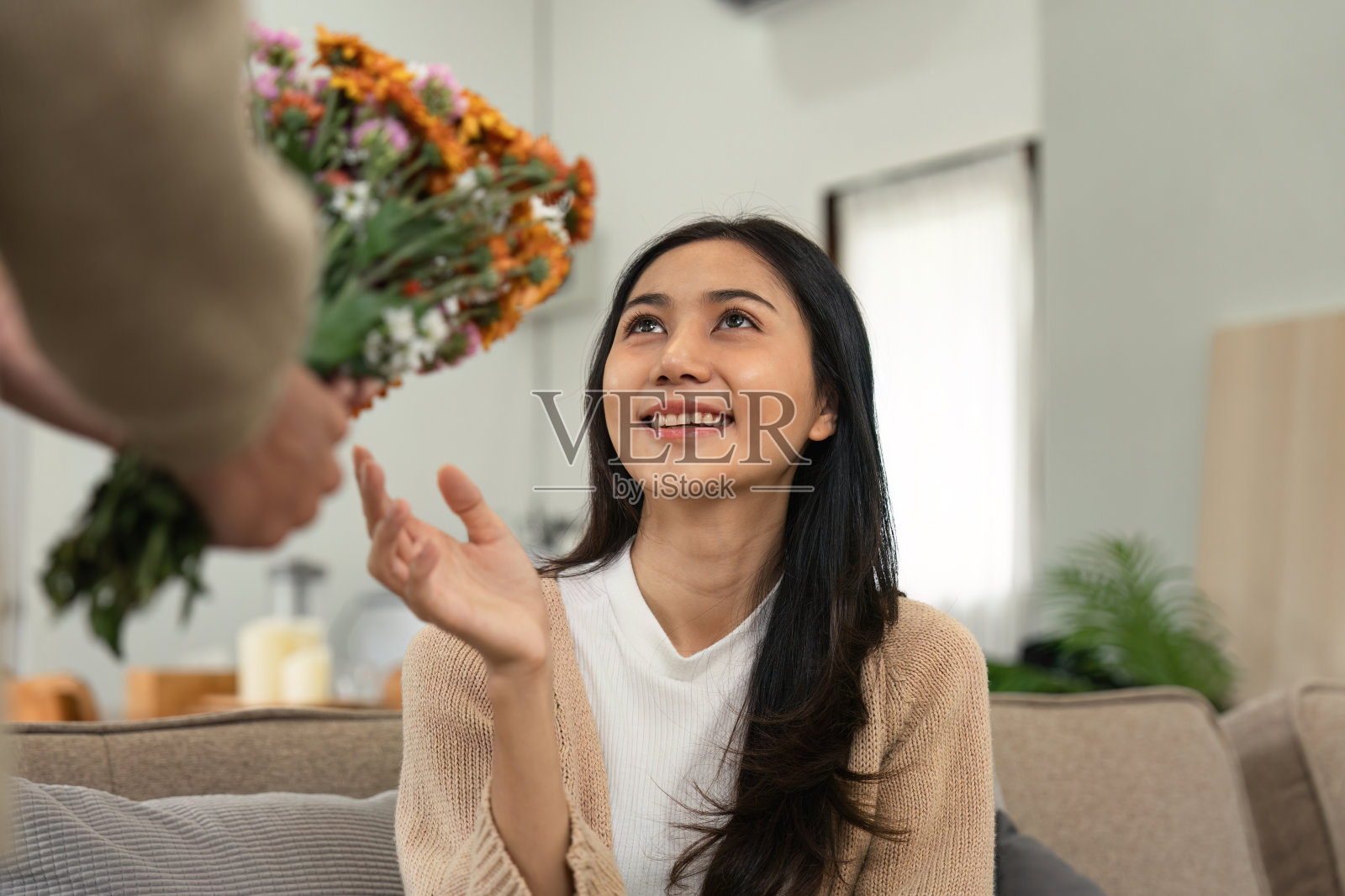 浪漫的夫妇在家里与鲜花，女人微笑和伸出手，舒适的室内设置，爱和幸福照片摄影图片