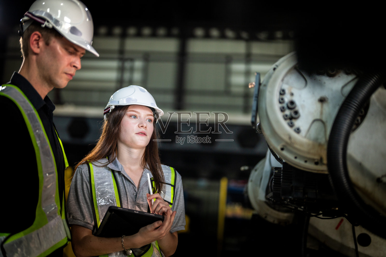 工厂工程师检查机器。自信团队成熟的商人用笔记本电脑站在工业机械臂旁，商人高空检测生产电子零件装置的技术。照片摄影图片