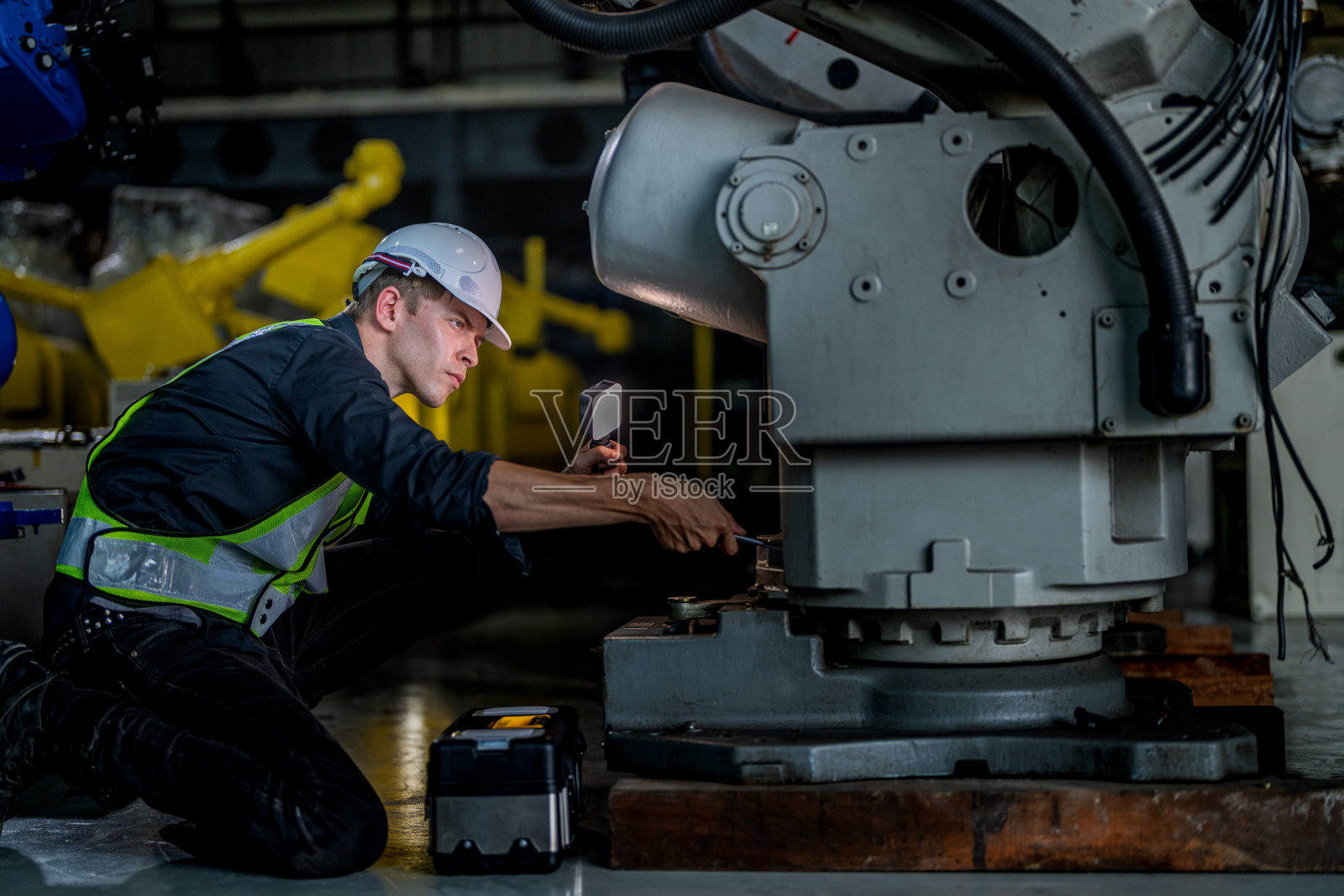 在一家工厂里，男工程师正在维护自动机械臂机。工人检查和修理自动机械手。技术员检查工厂机器的维修情况。照片摄影图片