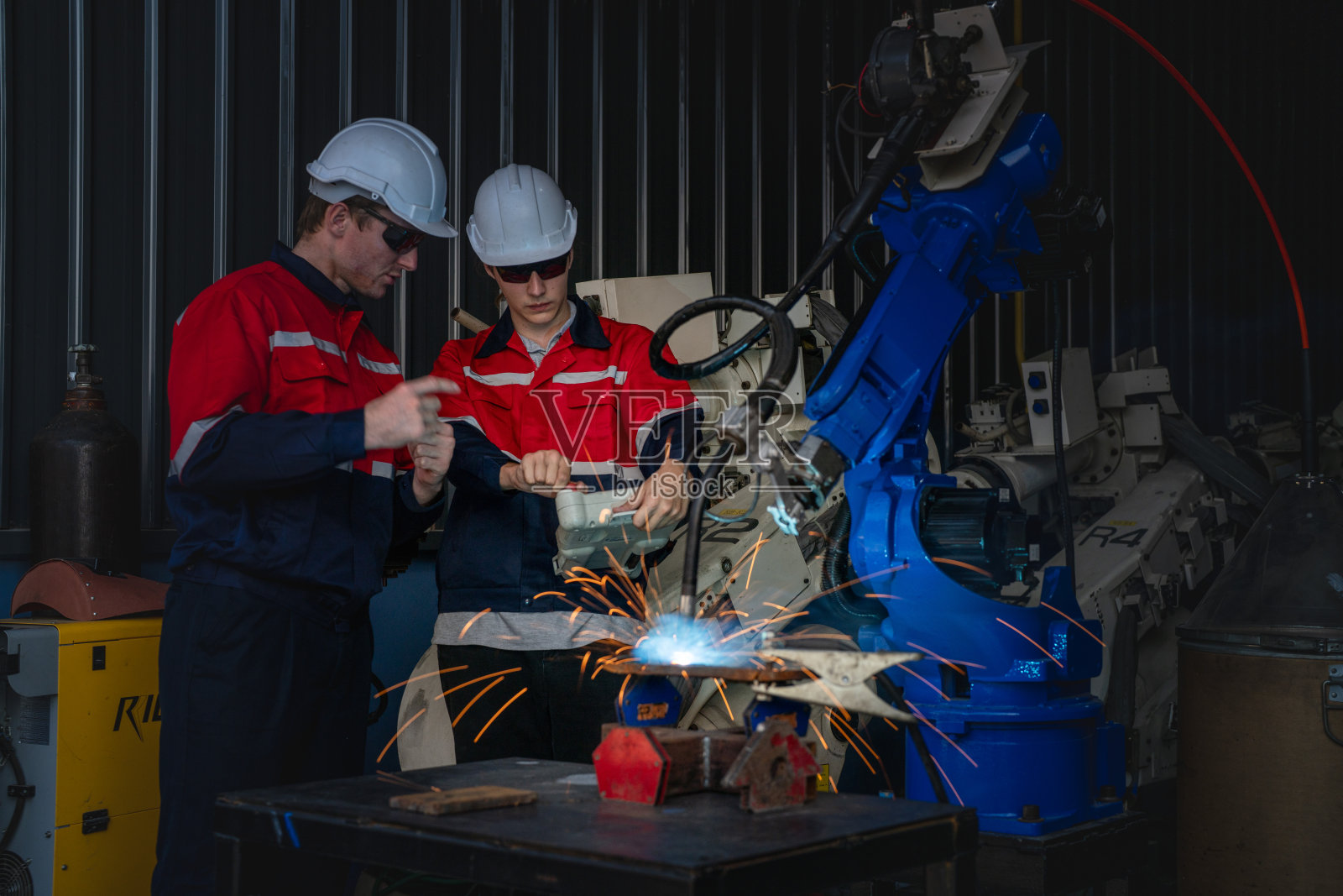 在一家工厂里，男工程师正在维护自动机械臂机。工人检查和修理自动机械手。技术员检查工厂机器的维修情况。照片摄影图片