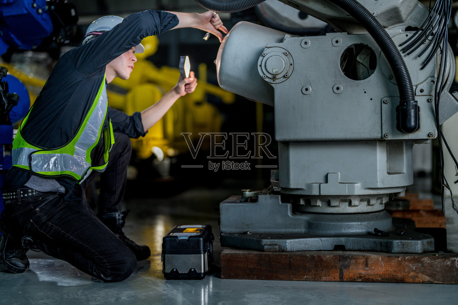 在一家工厂里，男工程师正在维护自动机械臂机。工人检查和修理自动机械手。技术员检查工厂机器的维修情况。照片摄影图片