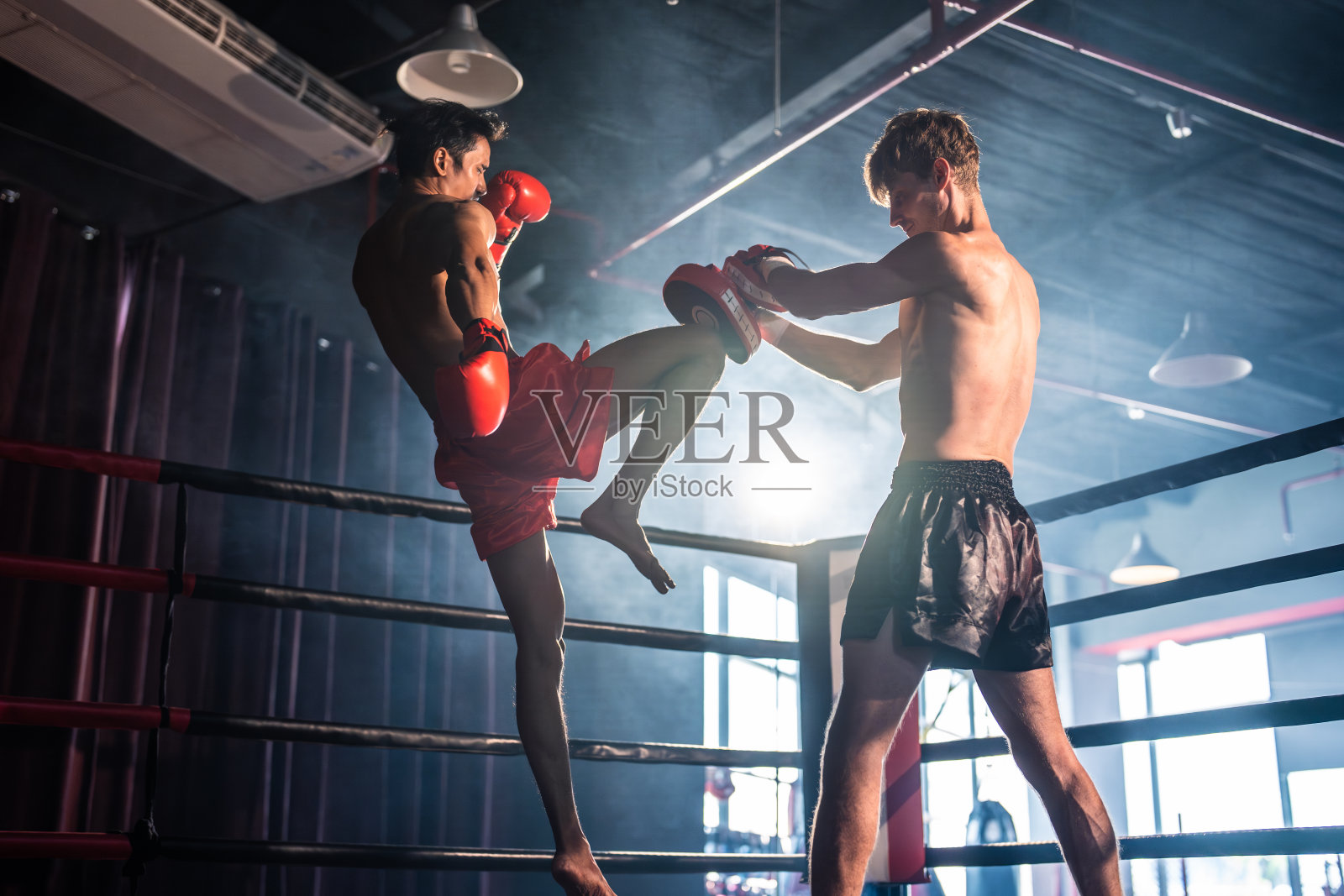 两个年轻的职业拳击手正在舞台上进行比赛。有魅力的男性运动员，肌肉发达，赤膊出拳，打对手，享受拳击运动在体育场的环。照片摄影图片