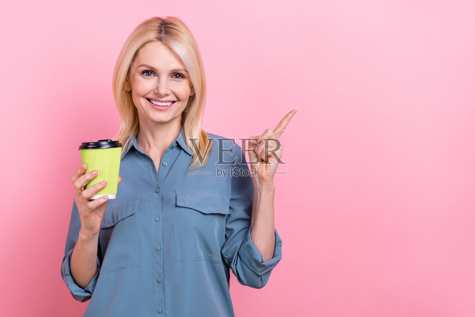 中年促销员的照片女商人经纪人拿着塑料杯喝直接手指模拟玛奇朵拿铁品牌孤立在粉红色的背景照片摄影图片