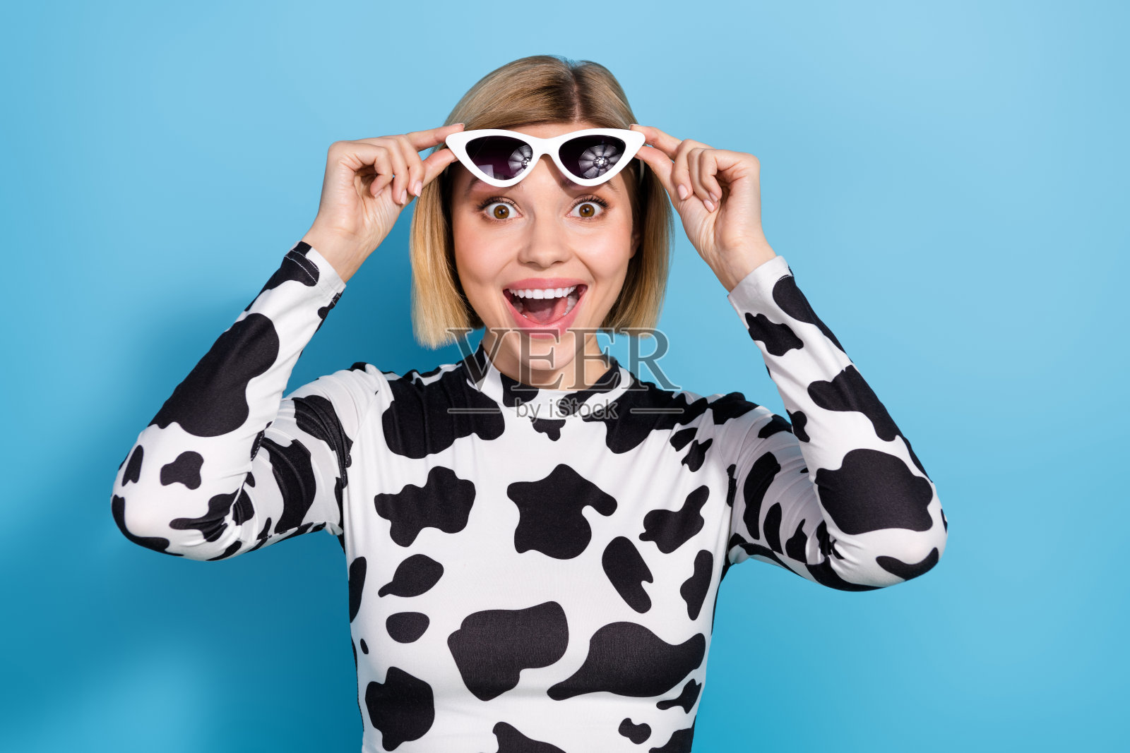 照片中惊讶的积极的女孩双手触摸太阳镜张开嘴不能相信孤立在蓝色的背景照片摄影图片