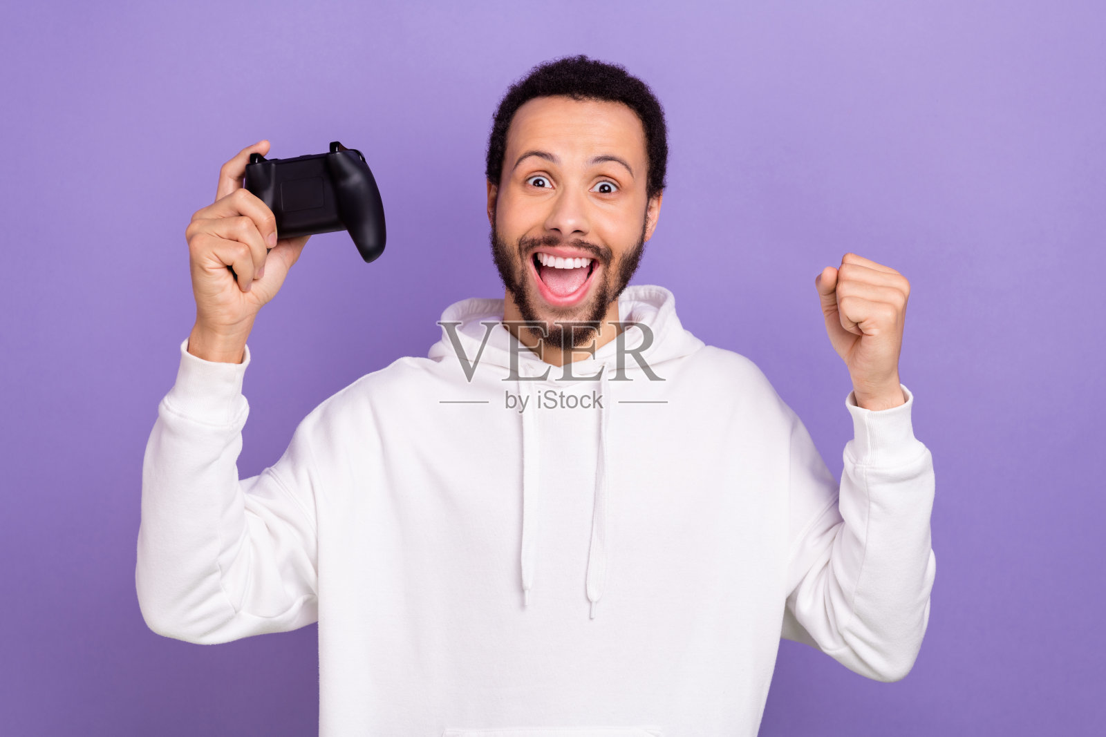 疯狂的喜出望外的人的肖像拿着控制器举起拳头视频游戏冠军成功孤立在紫色的背景照片摄影图片