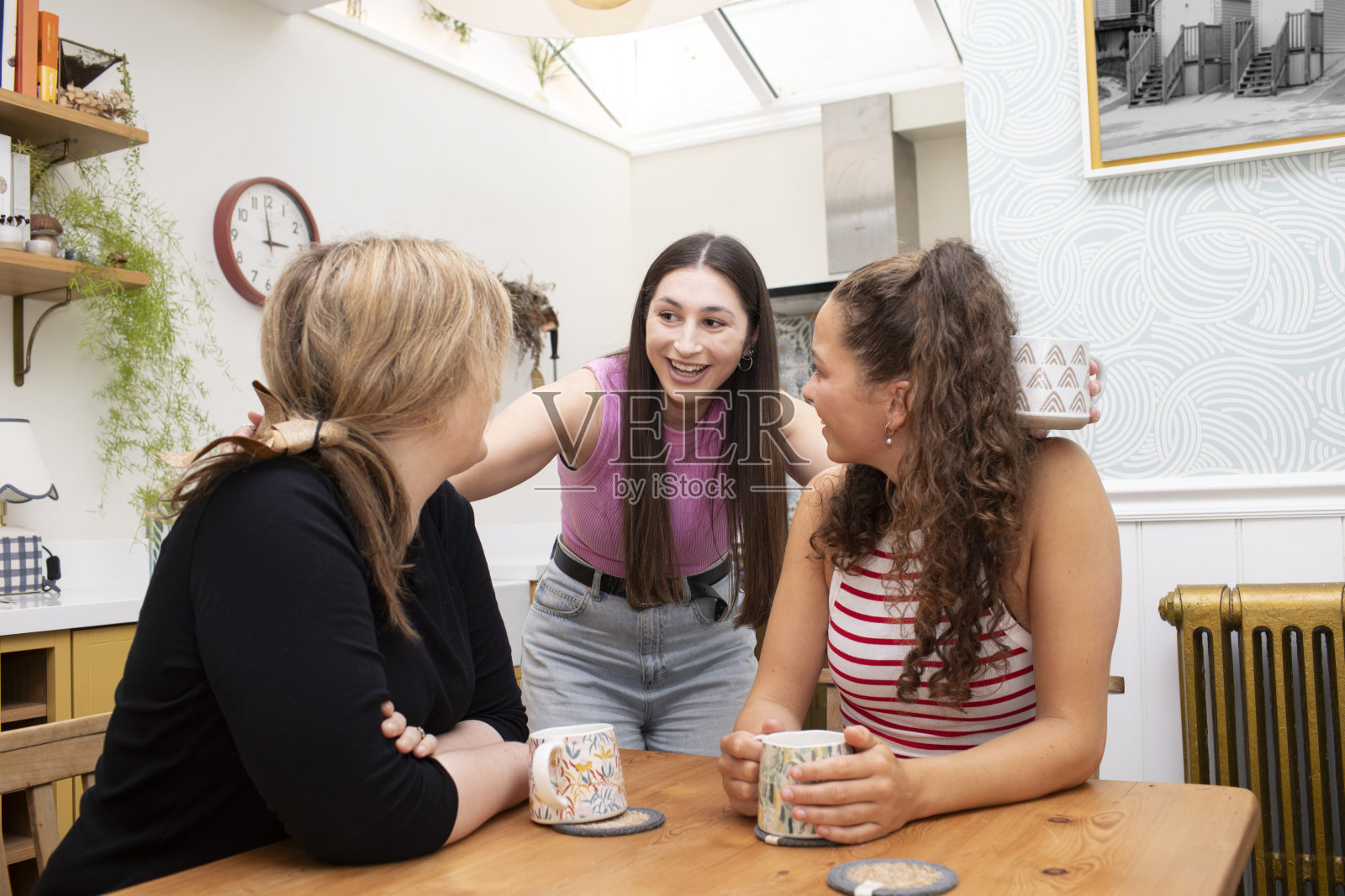 三个愉快的朋友在厨房的桌子旁聊天照片摄影图片