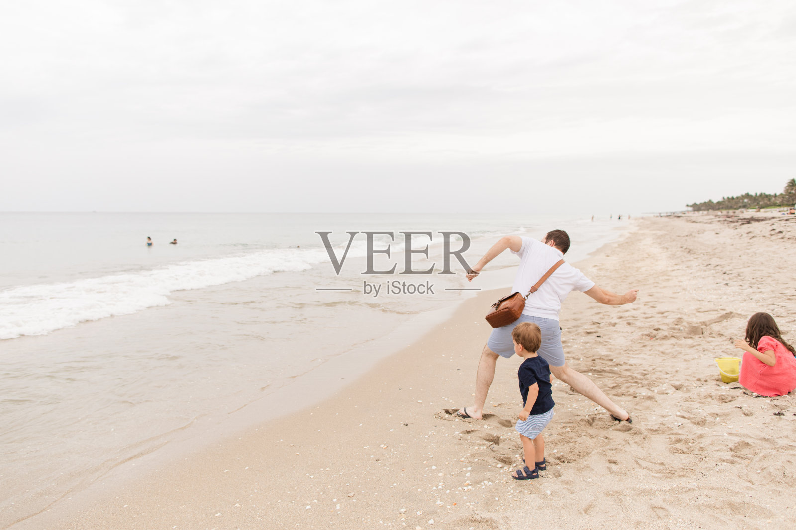 一个33岁的棕色短发的美国男人在宁静，光滑的海滩海岸线上跳过岩石和贝壳，同时带着他的两个孩子在一个宁静多云的夏日海滩日中午在佛罗里达州棕榈滩照片摄影图片