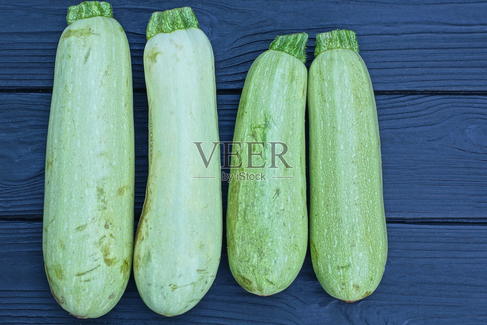 黑色木桌上放着新鲜的绿色大西葫芦照片摄影图片
