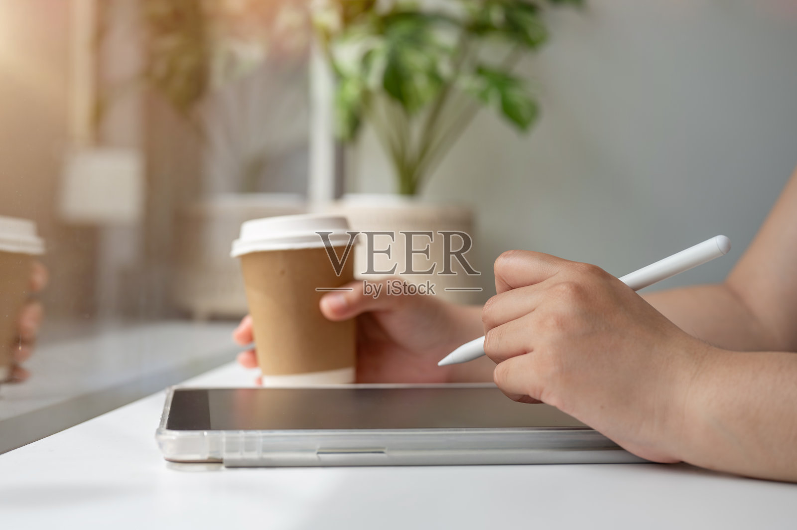 一个女人拿着一支手写笔，在一个数字平板电脑上写字，在咖啡店远程工作。照片摄影图片