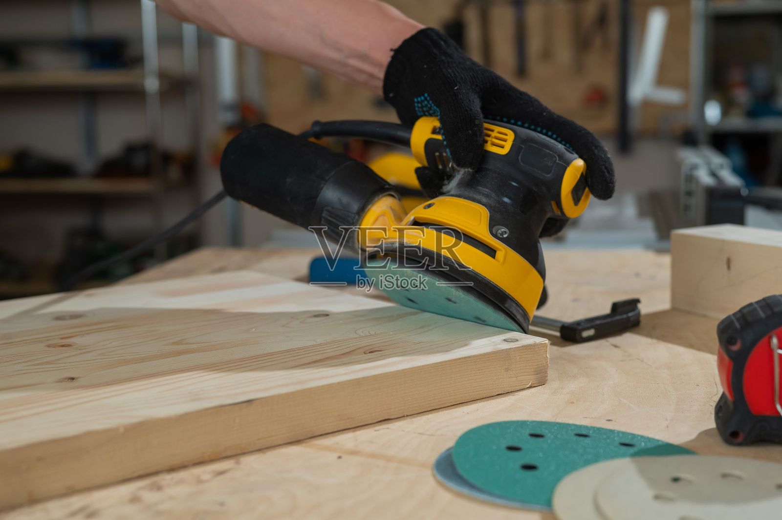 一个人在车间里使用轨道磨砂机。木匠手的特写。照片摄影图片